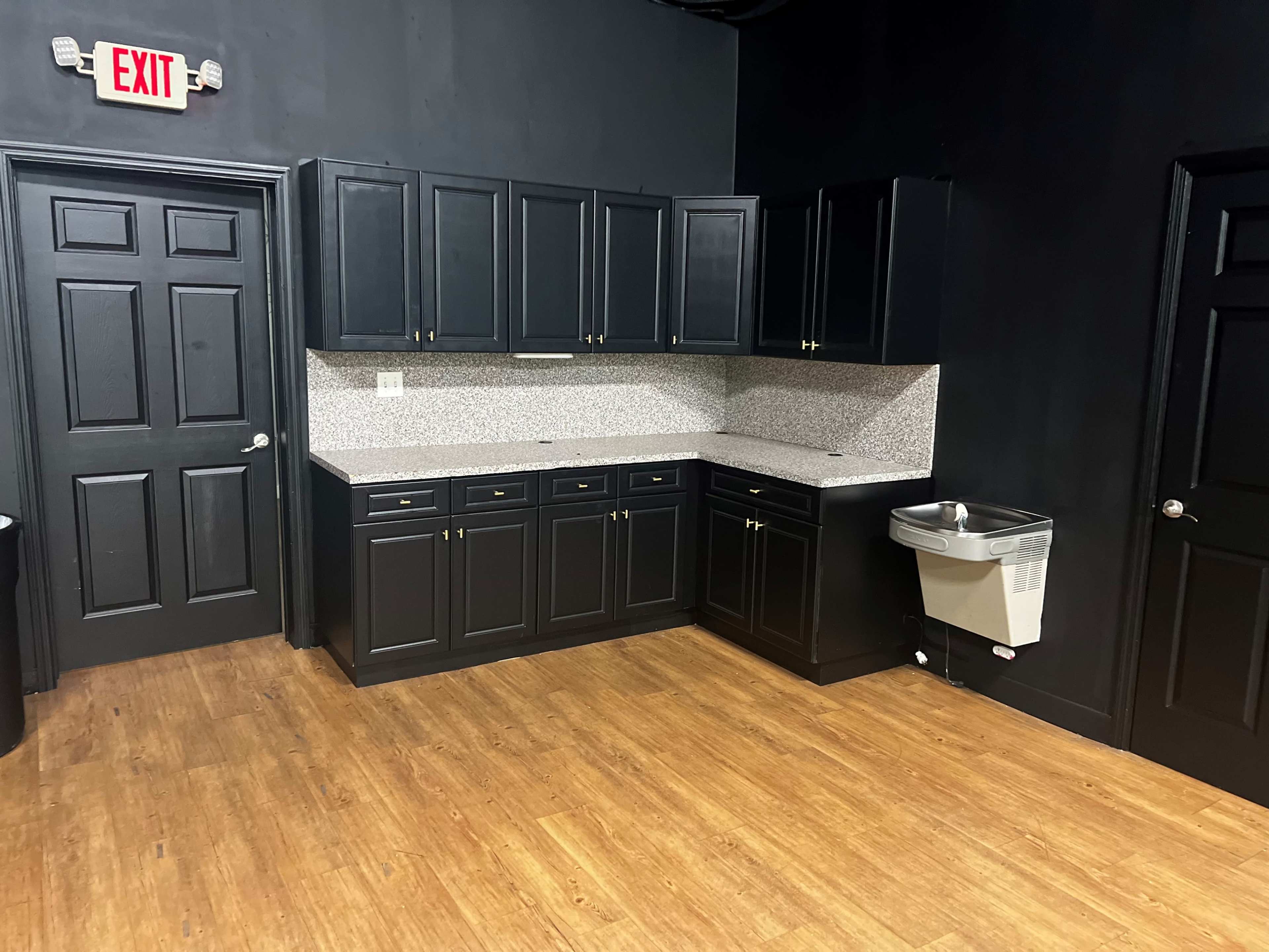 A kitchen with black cabinetry, a speckled countertop, and a metal sink against a dark wall.