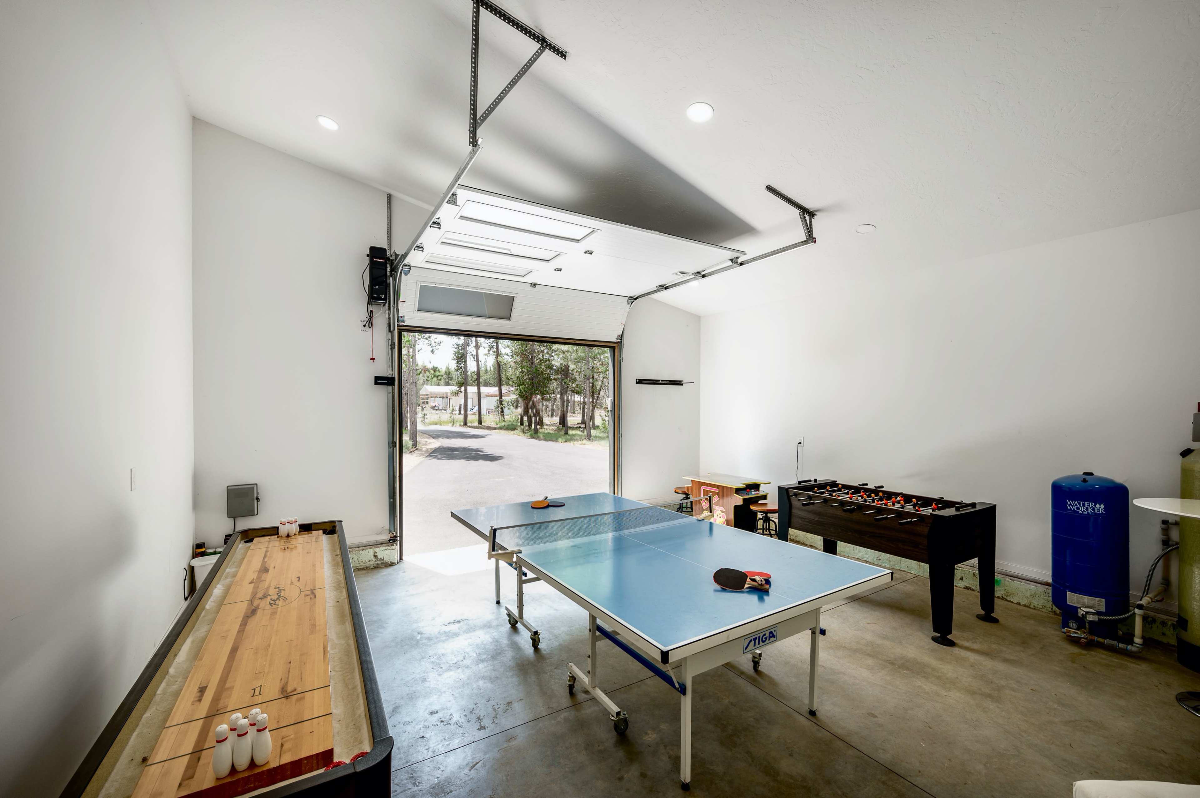 A spacious garage features a ping pong table, a foosball table, and a long wooden table along one wall.
