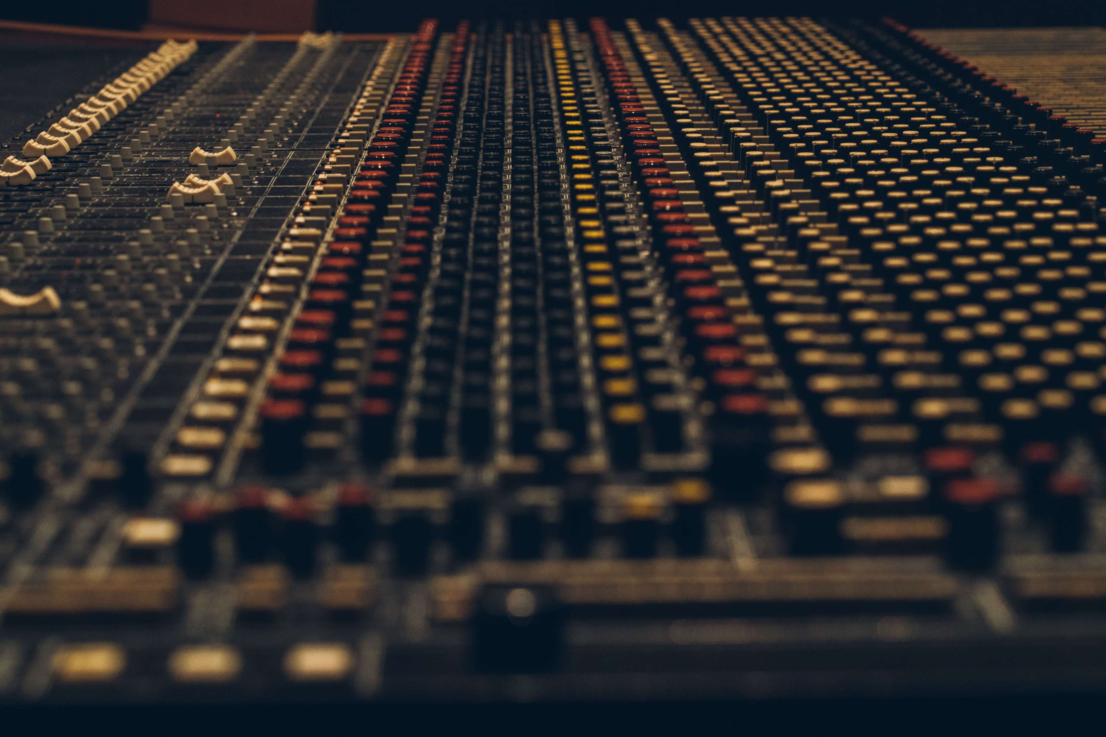 A close-up of a sound mixing console with numerous colorful knobs and sliders arranged in rows.