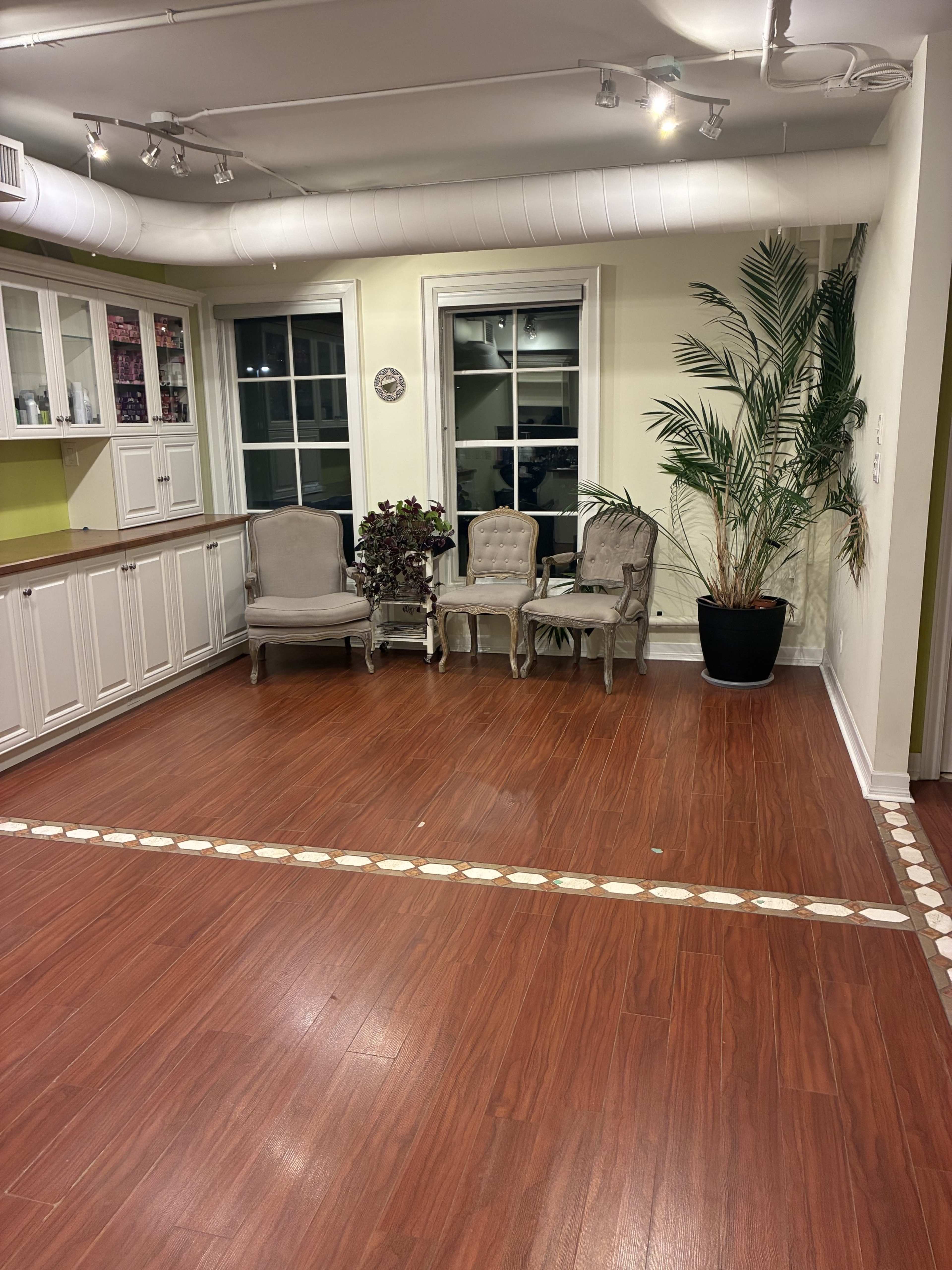 The image shows a spacious room with wooden flooring, featuring three upholstered chairs, a potted plant, and a long white line along the floor.
