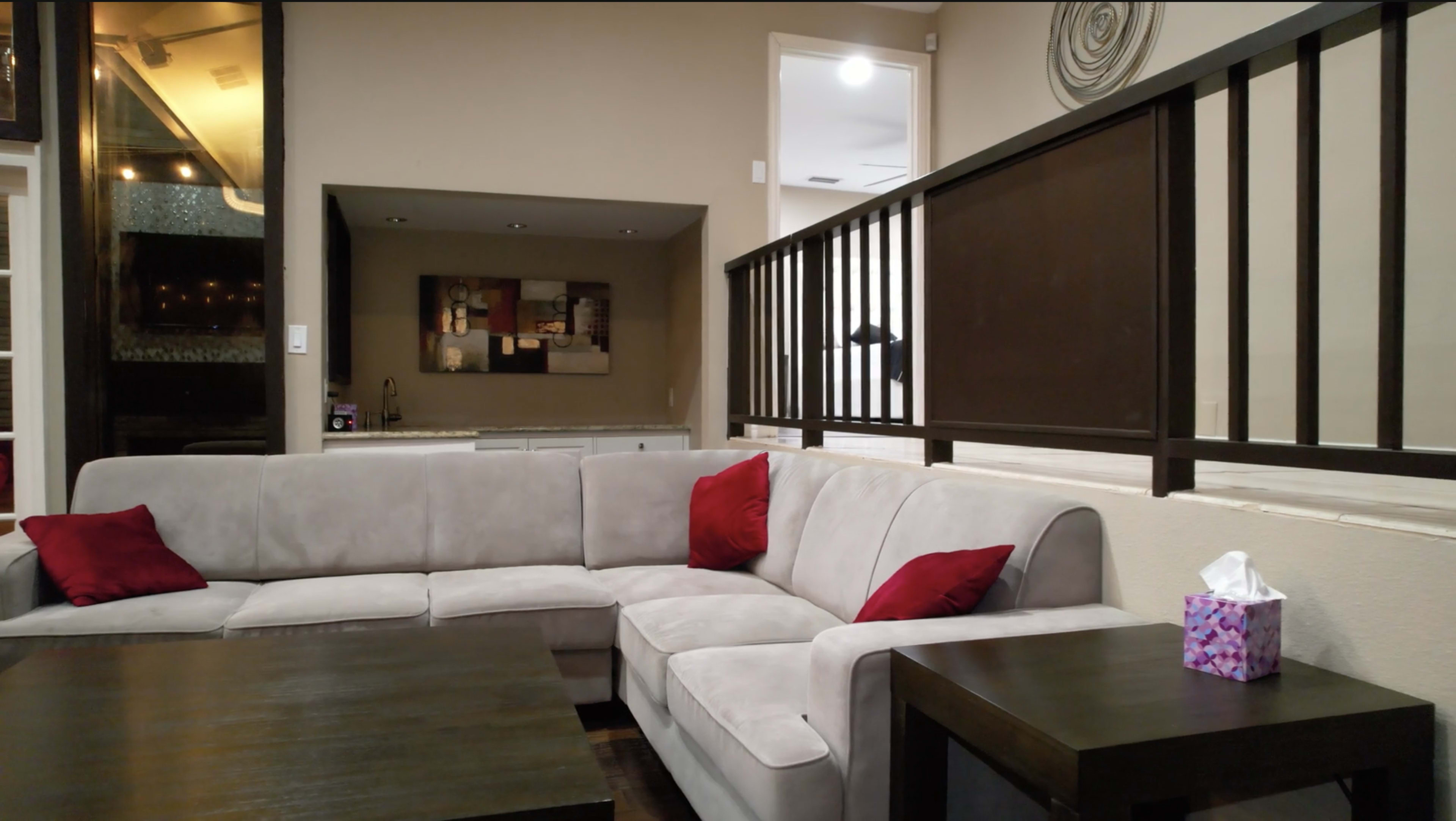 A modern living room features a sectional sofa with red cushions, a dark wooden coffee table, and a decorative railing in the background.