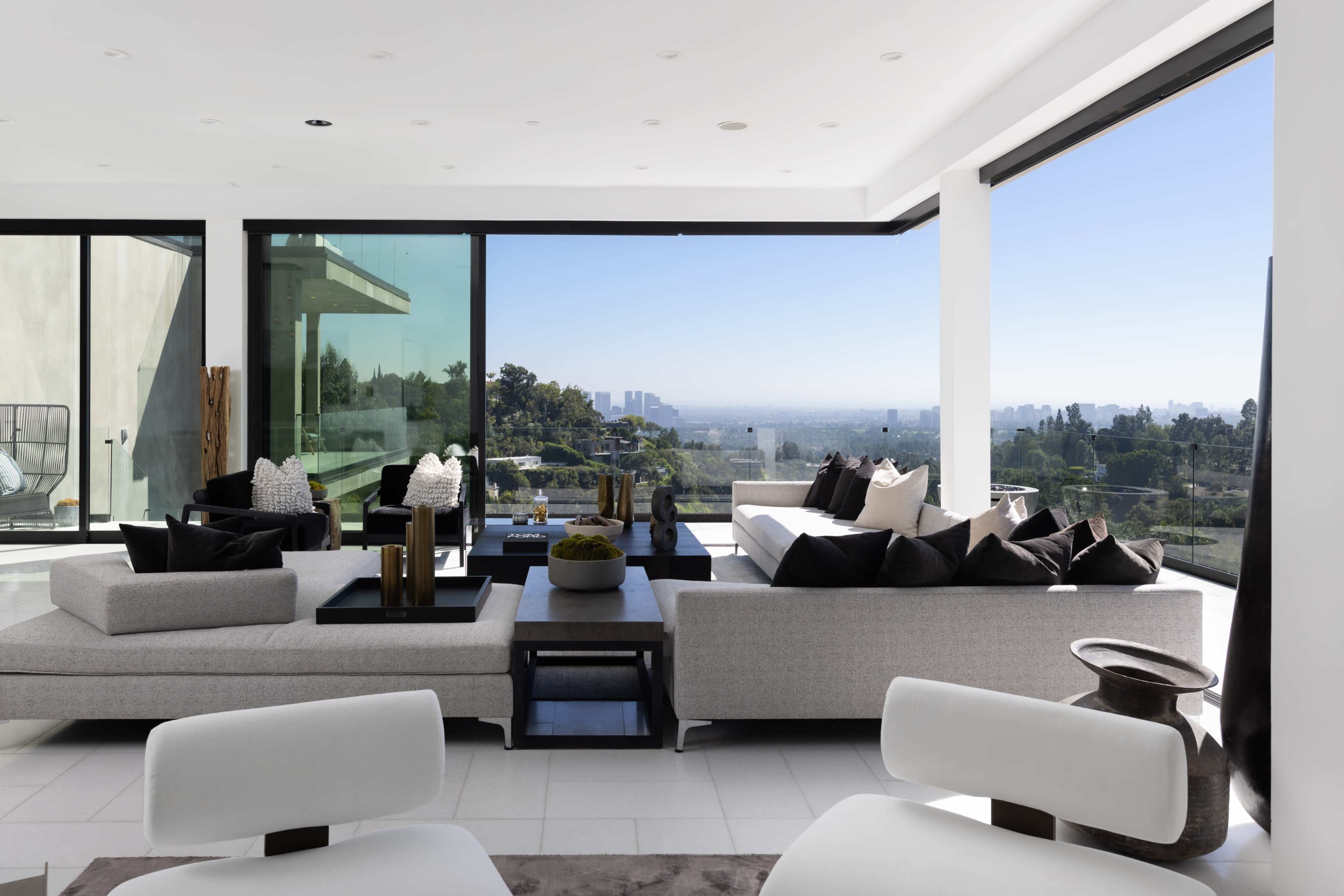 A modern living room with large windows overlooking a city view, featuring contemporary furniture and a neutral color palette.