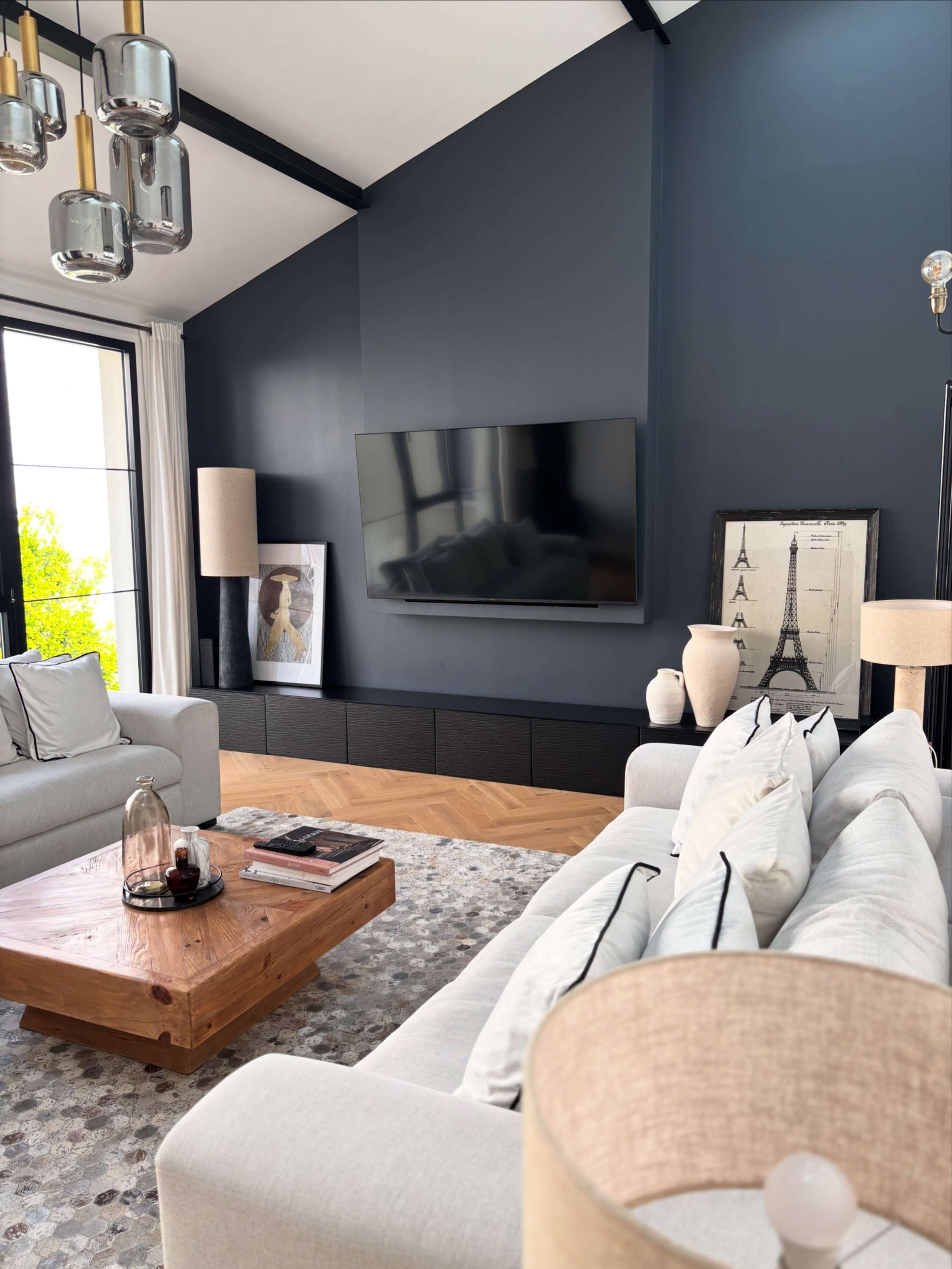 The image depicts a modern living room featuring a dark blue accent wall, a flat-screen television, a wooden coffee table, and decor including lamps and framed artwork.