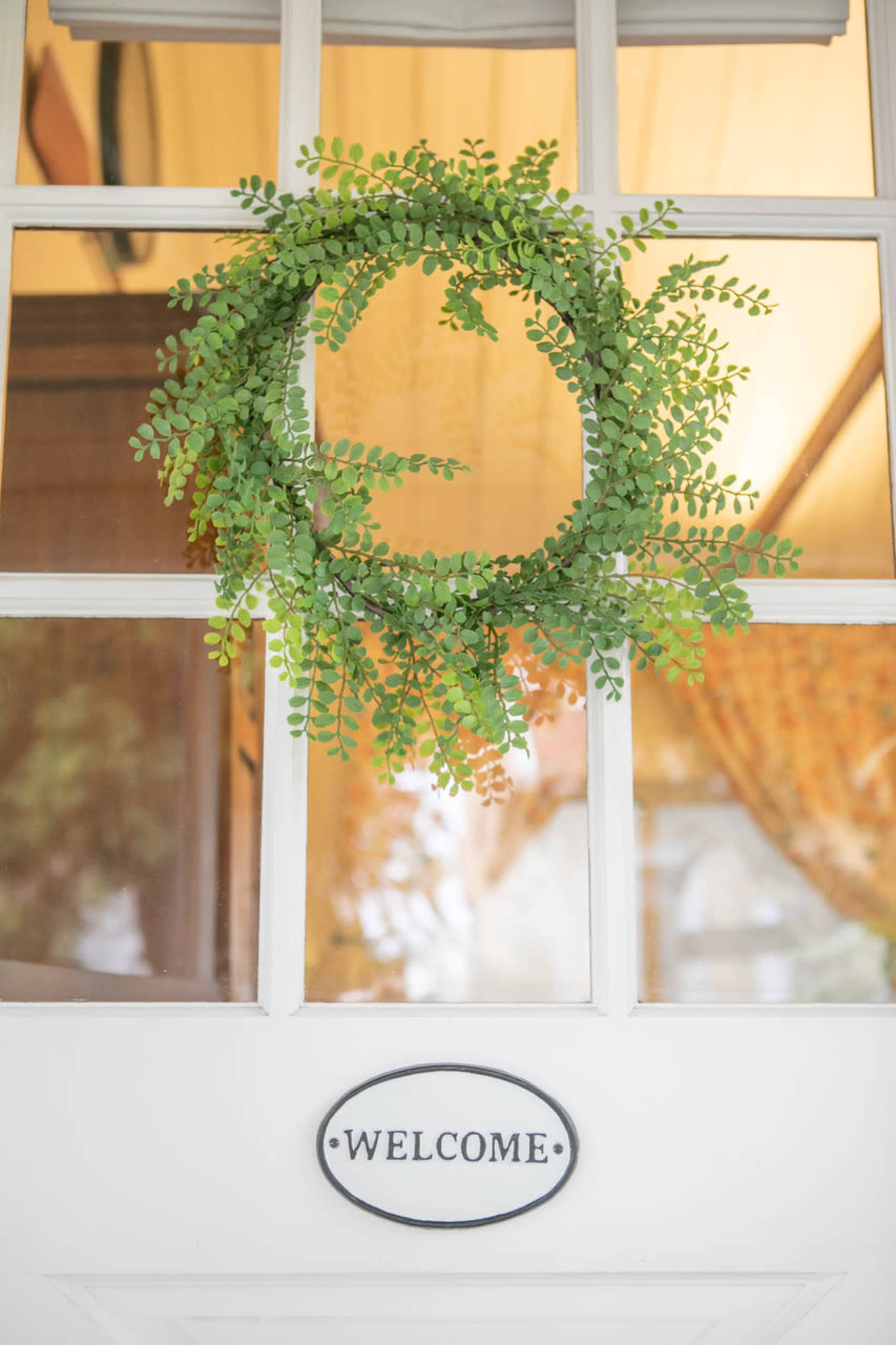 A green wreath hangs on a glass-paneled door with a "WELCOME" sign below it.