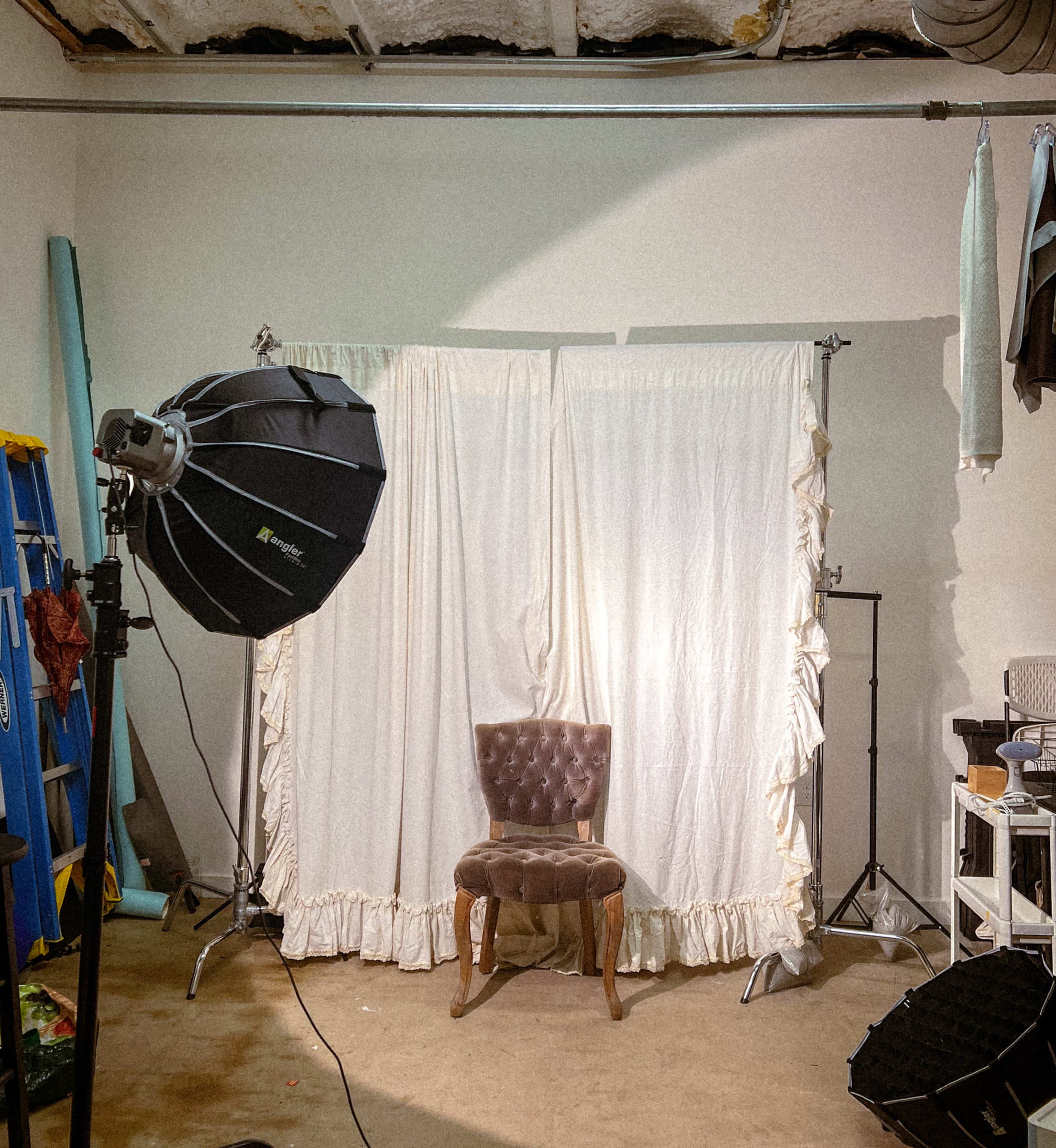 A photography setup featuring a single velvet chair in front of a white backdrop, accompanied by a large softbox light.