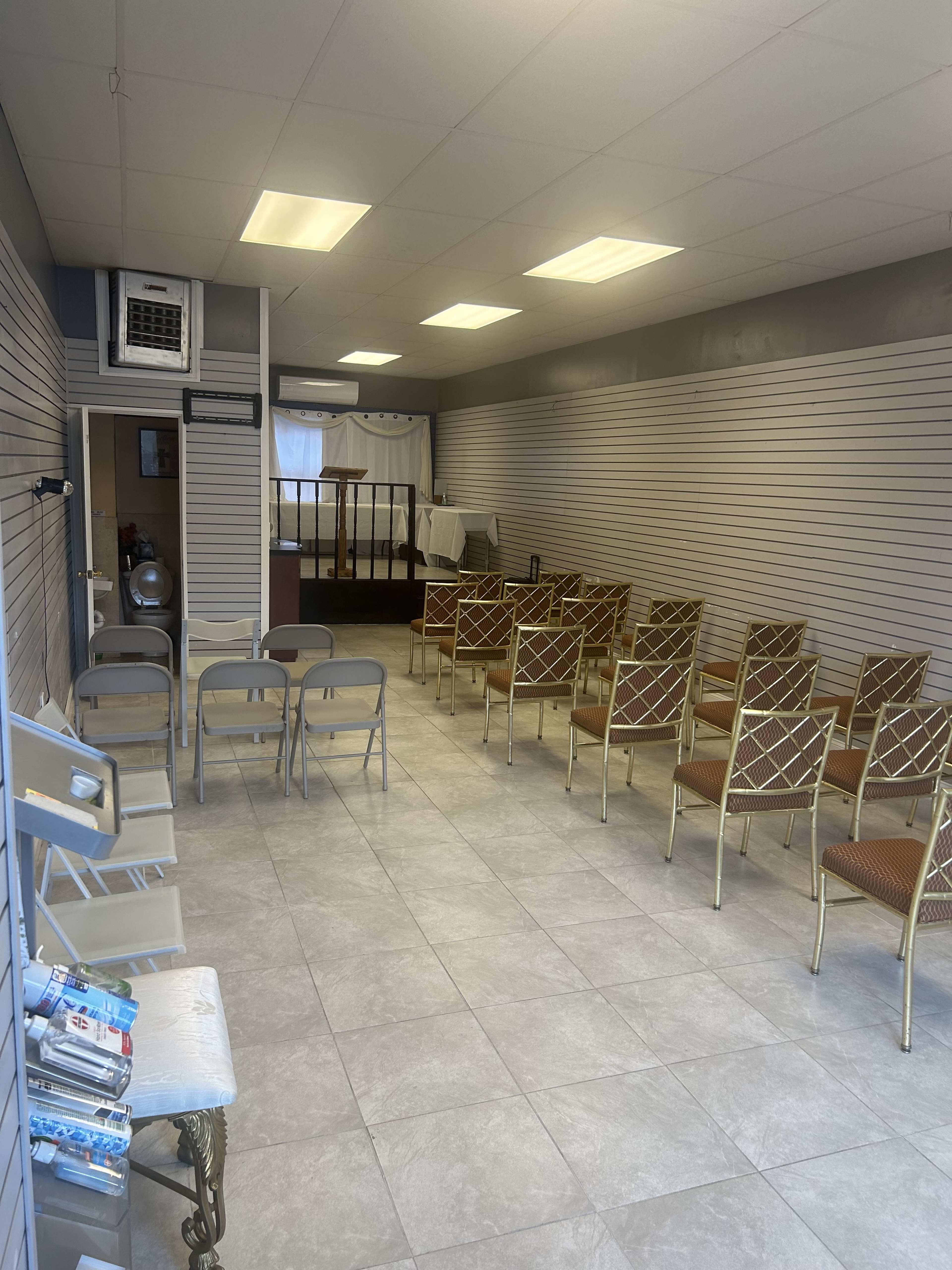 A spacious interior of a room with rows of chairs arranged for seating, and a small reception area visible at the back.