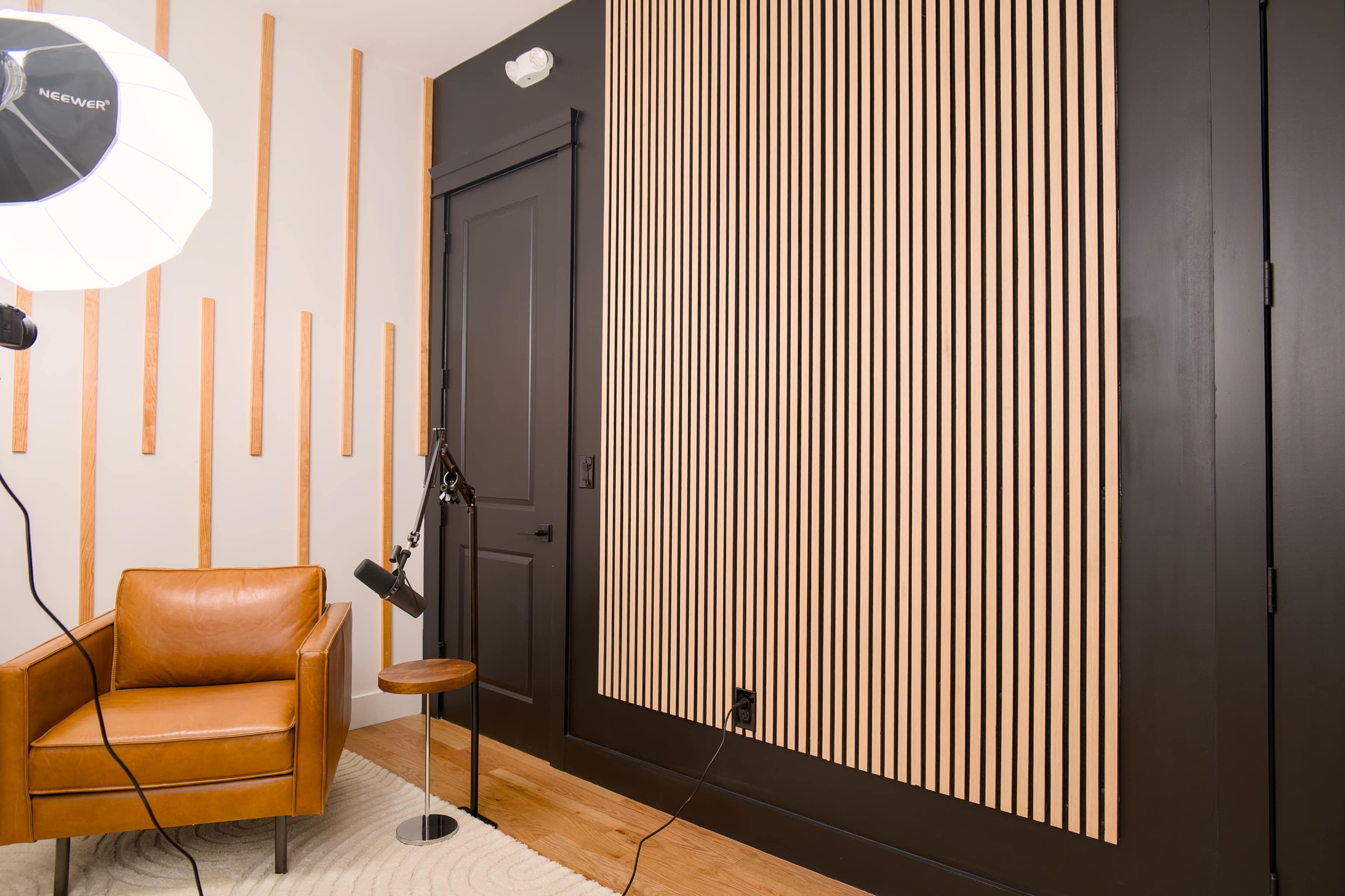 The image shows a modern room featuring a brown leather chair, a small black side table, and a wall with vertical wooden slats.