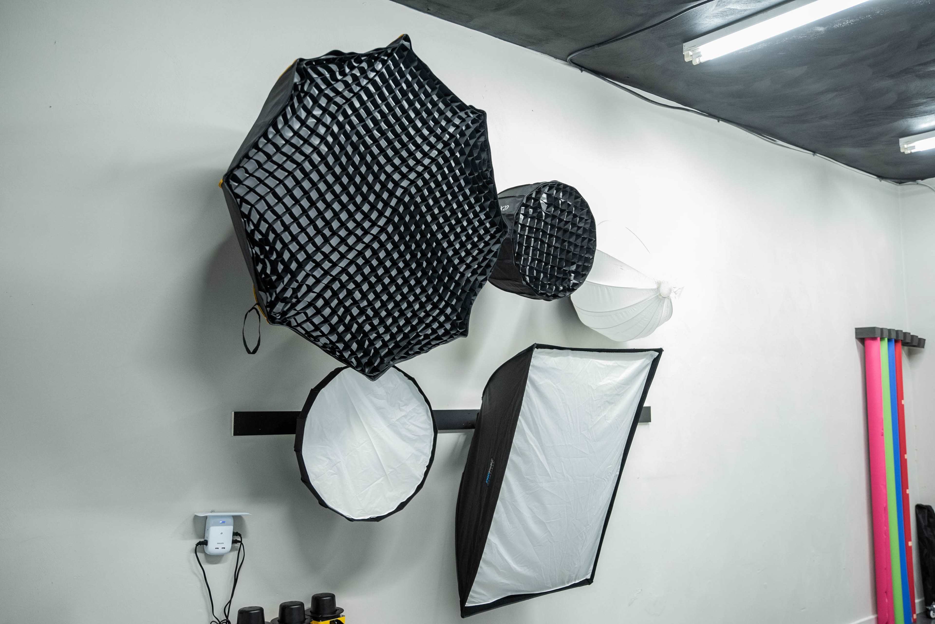 Several photography light modifiers, including softboxes and reflectors, are mounted on a wall in a studio.