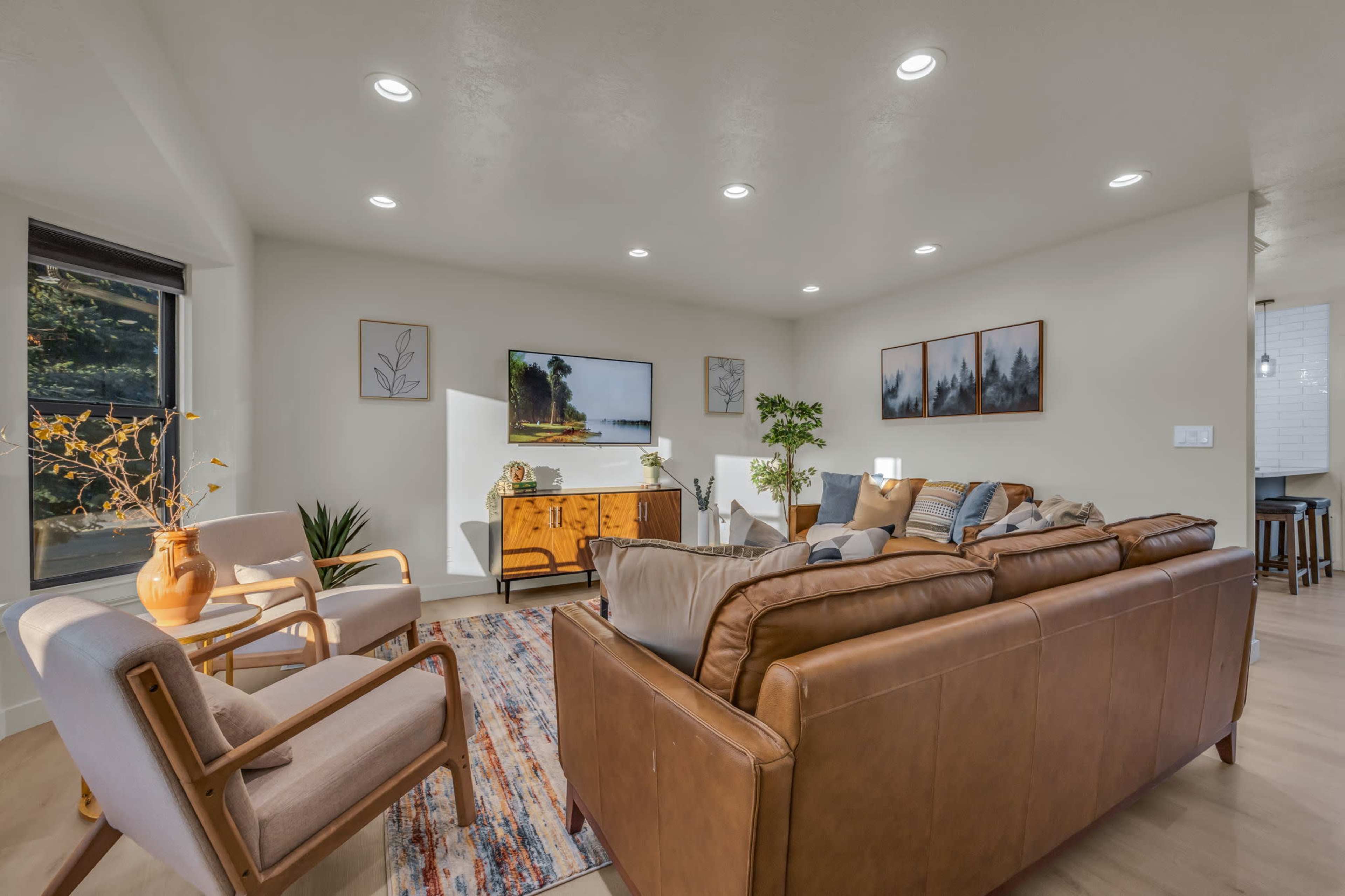The living room features a leather sofa, two armchairs, and a wooden sideboard, illuminated by recessed lighting and decorated with framed art.