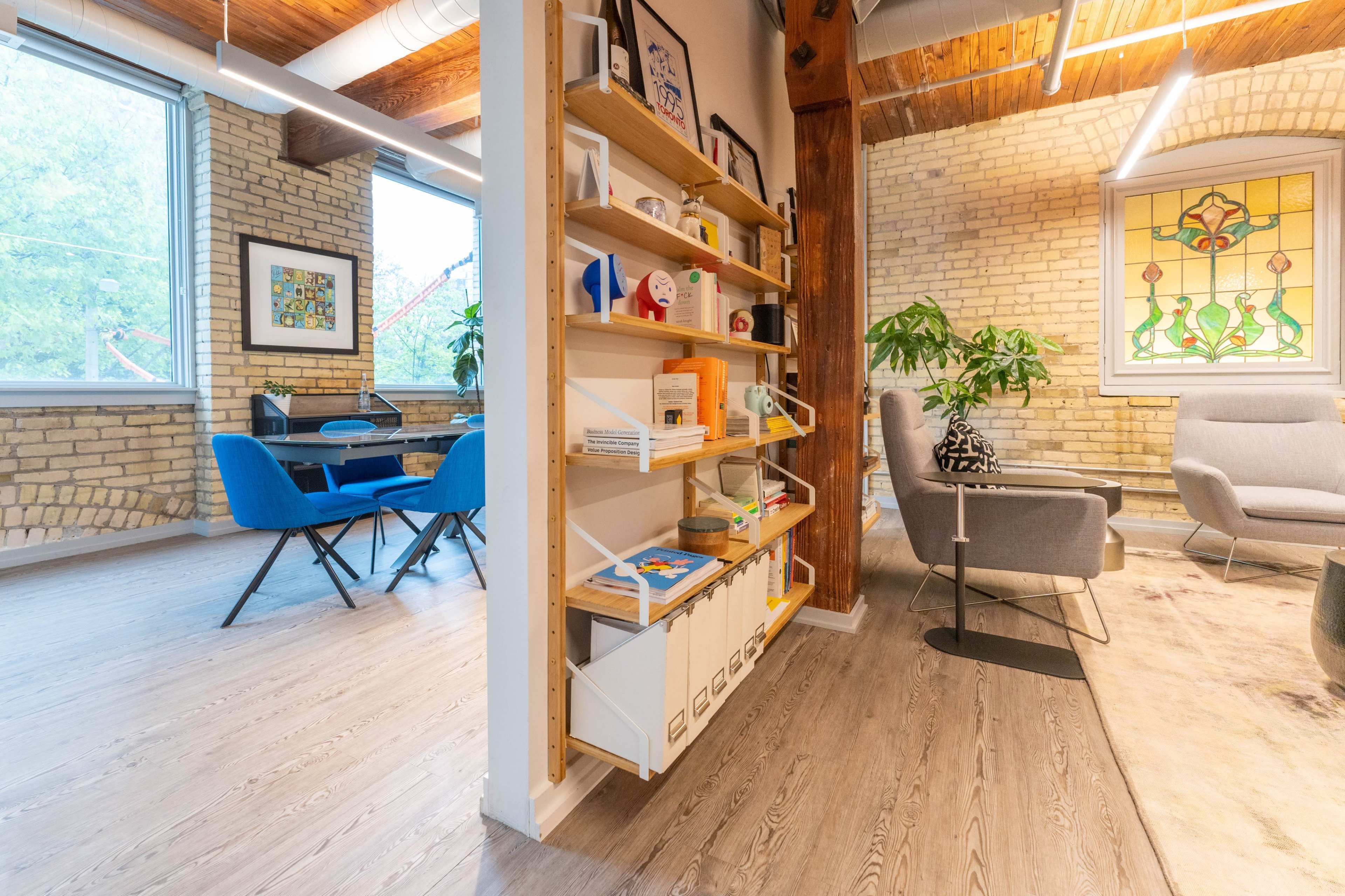 A modern interior space featuring a wooden shelving unit filled with various items, a seating area with gray furniture, and a dining area with blue chairs.