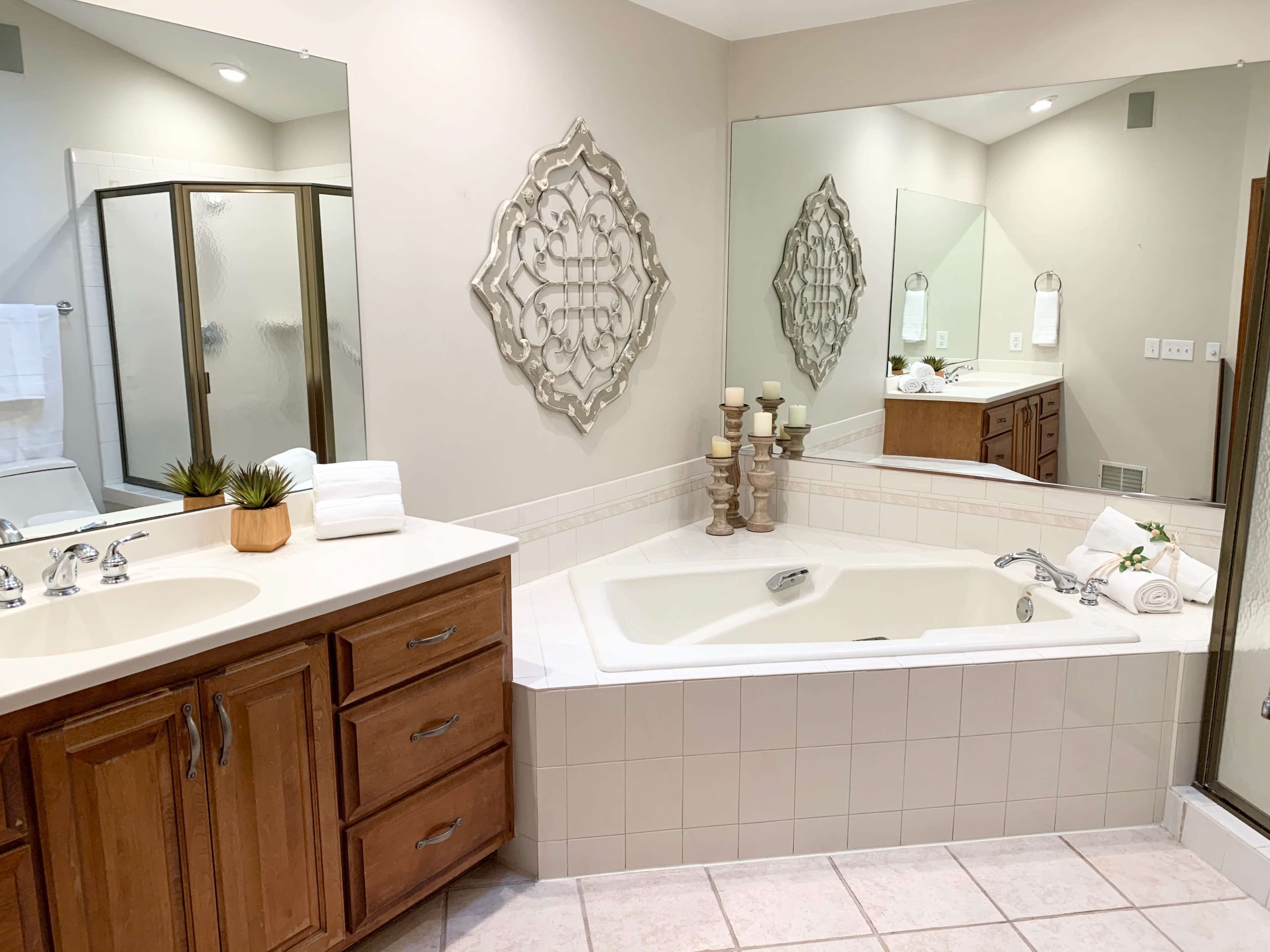 A well-lit bathroom featuring a large bathtub, double sinks with wooden cabinets, and a separate glass shower stall.