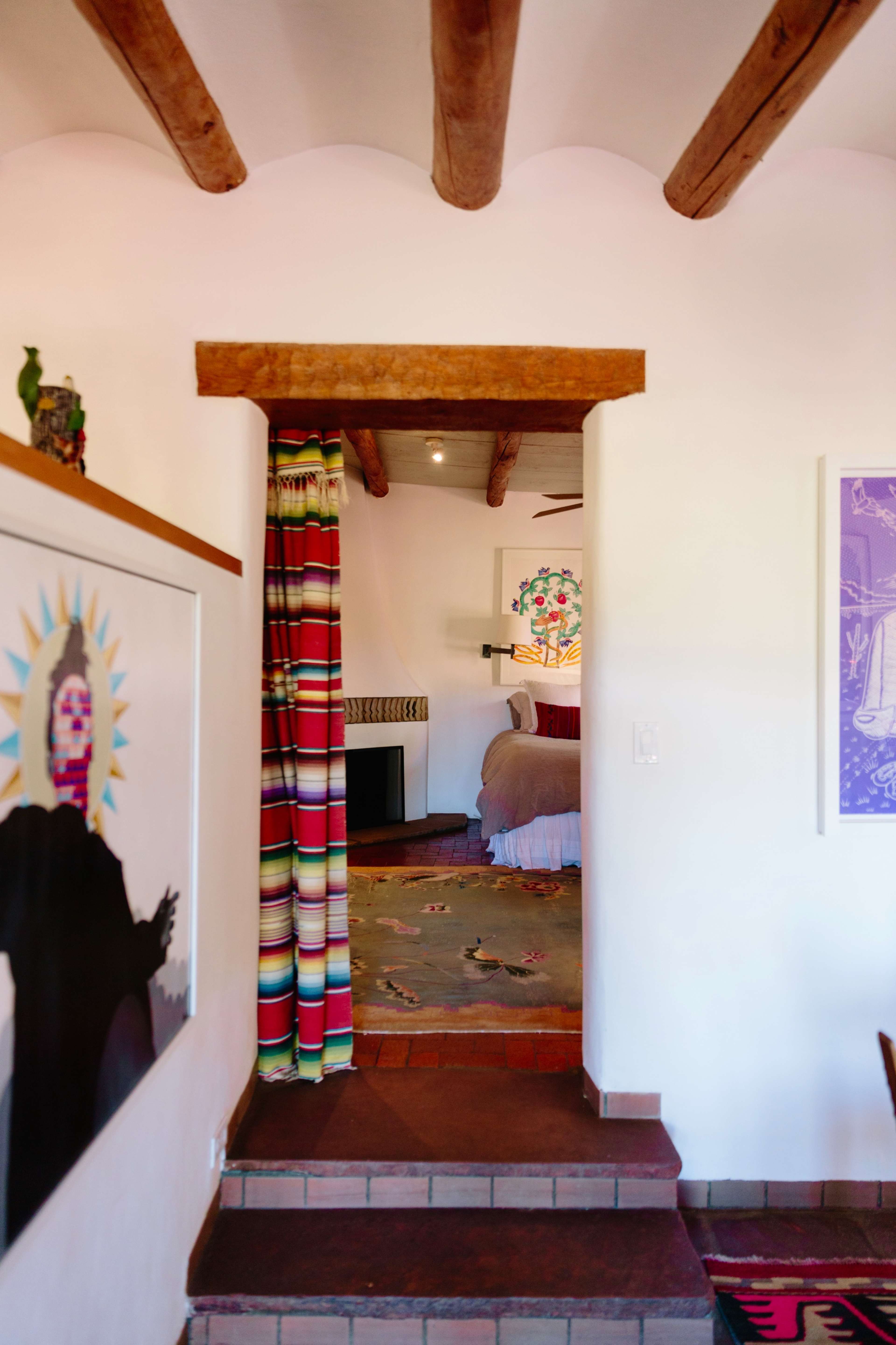 A colorful curtain separates a cozy room with wooden beams from a hallway adorned with artwork and a staircase.
