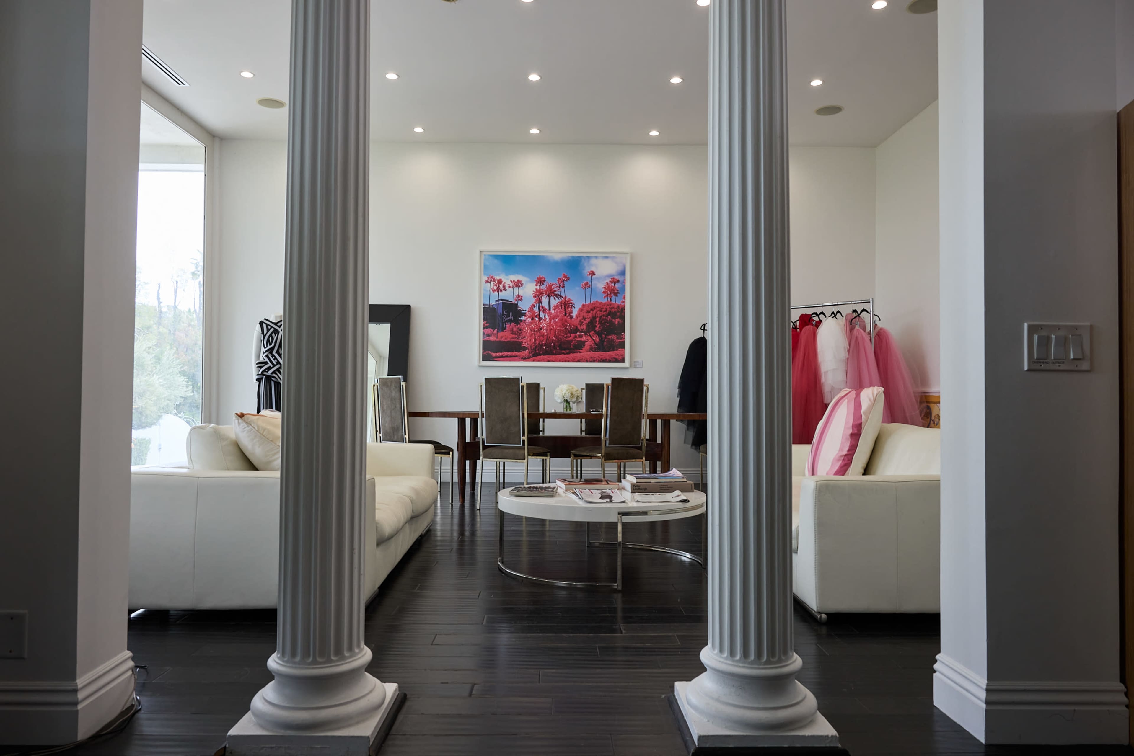 The image features a modern interior with white sofas, a dining table, and a large artwork, framed by two columns.