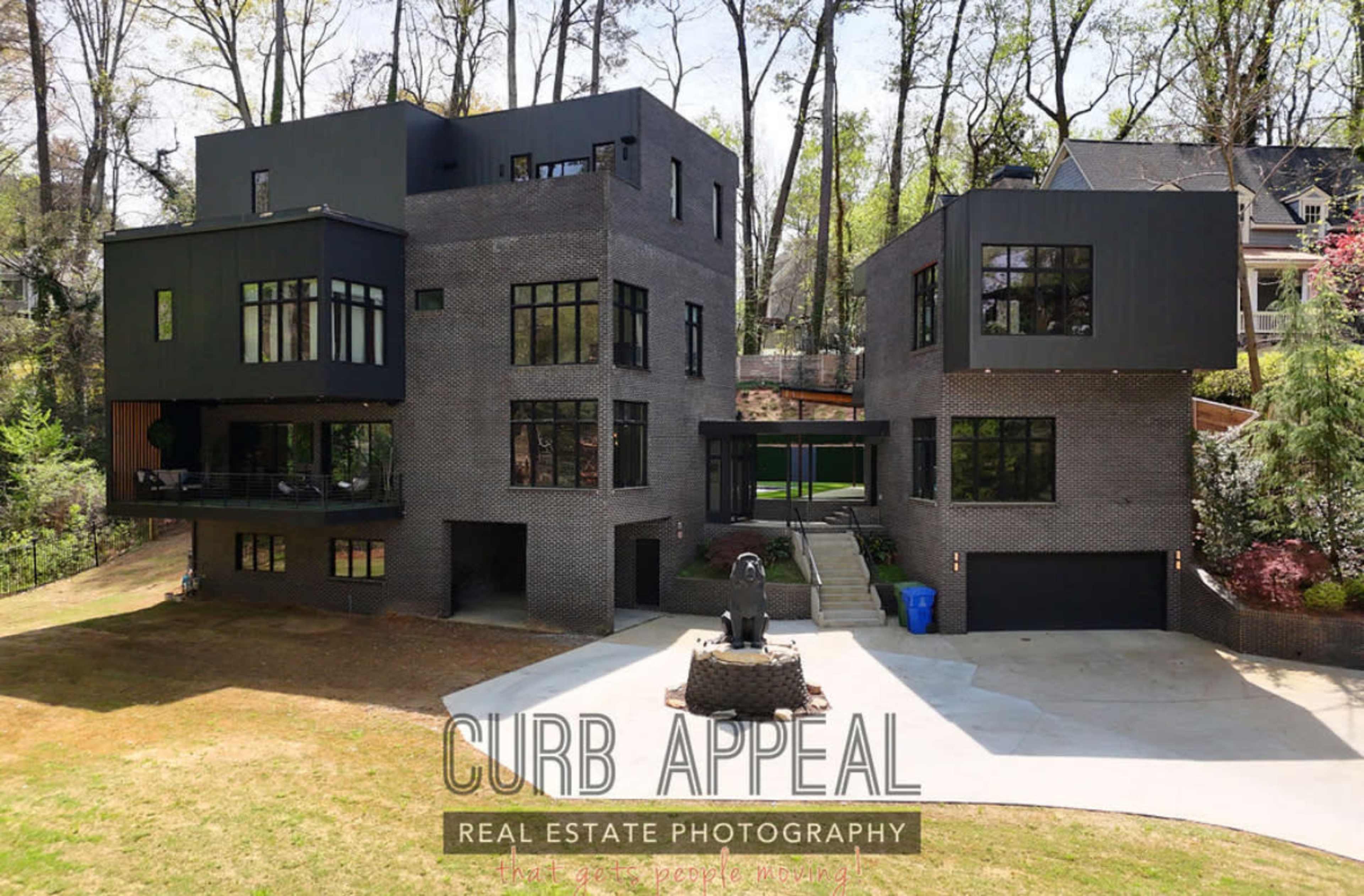 The image shows a modern two-story house with a unique geometric design and a black brick exterior, set on a landscaped lot.