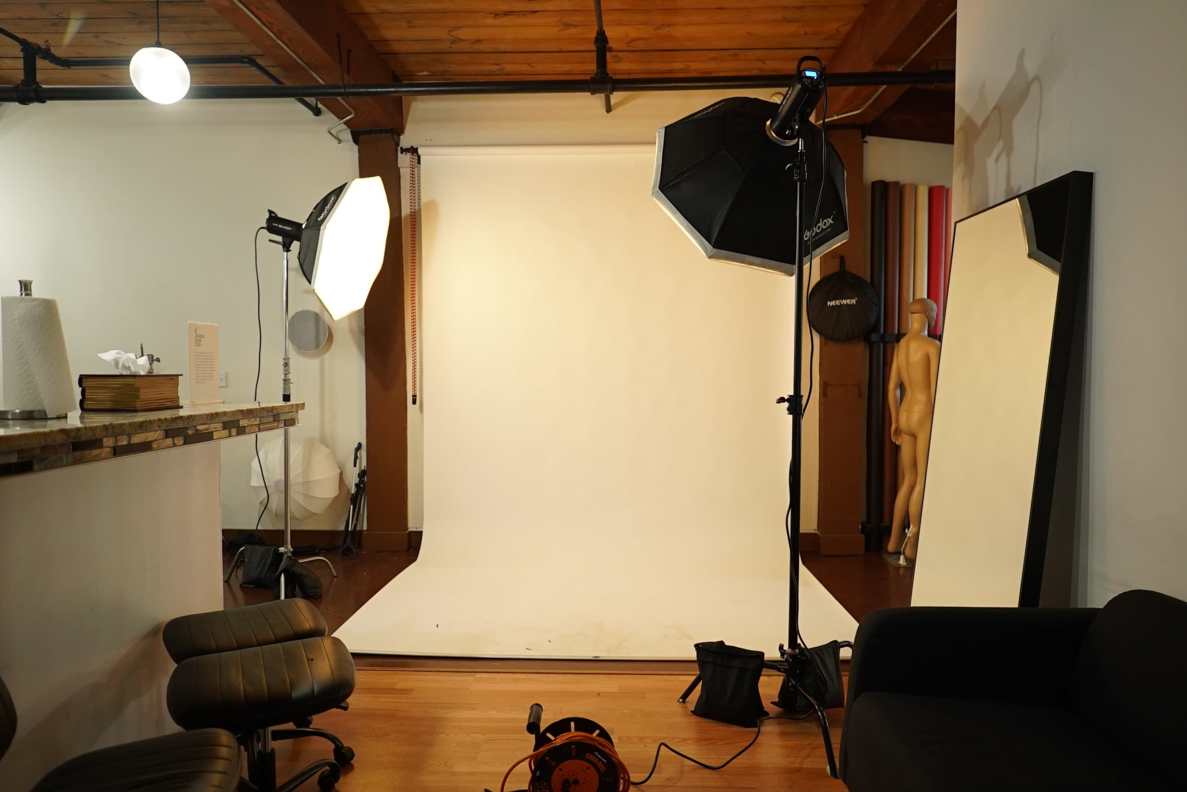 The image shows a photography studio with a plain backdrop, lighting equipment, and a model's mannequin positioned in the corner.