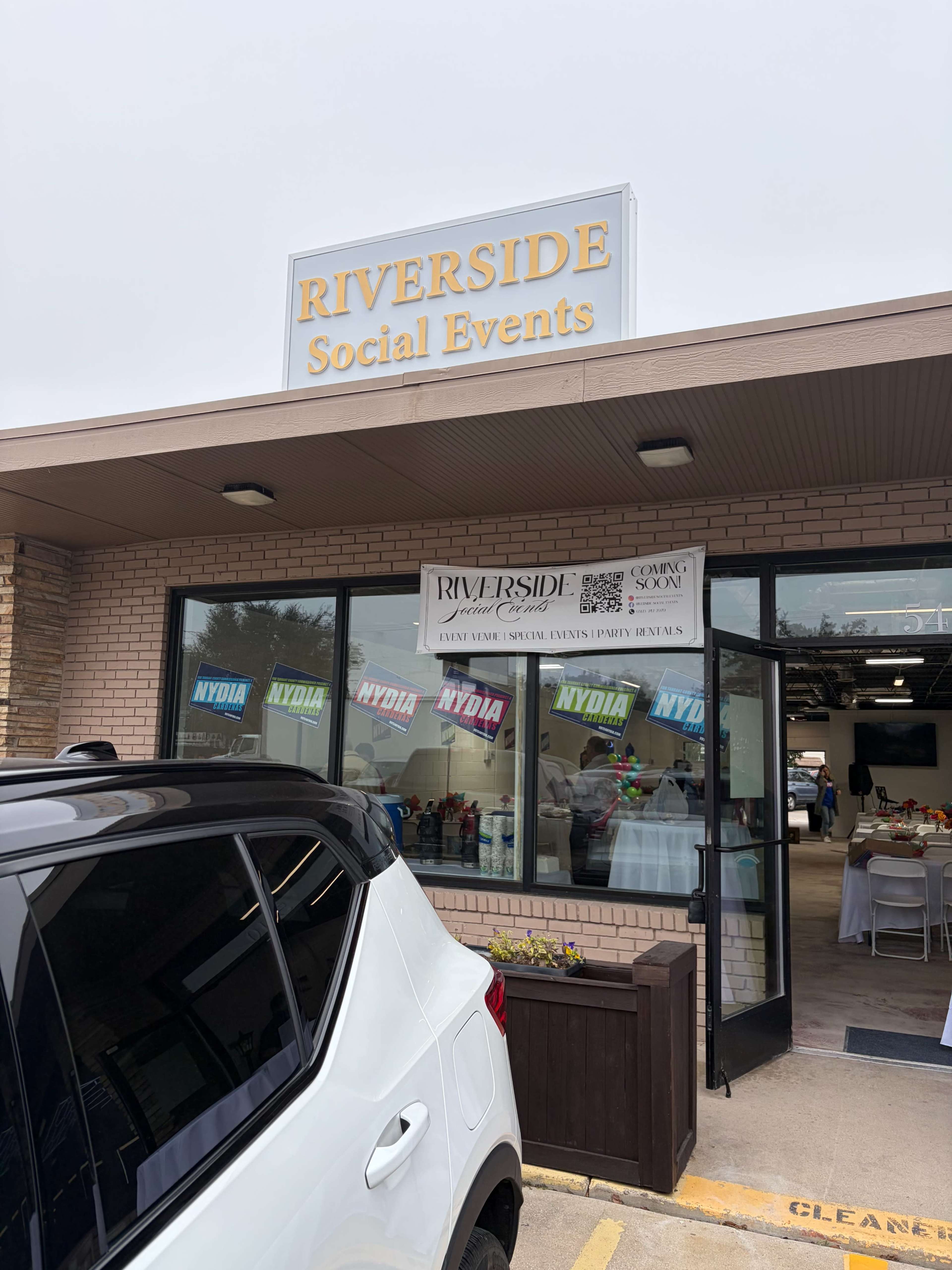 The image shows the entrance of a venue called "Riverside Social Events," featuring a sign above the door and a vehicle parked outside.