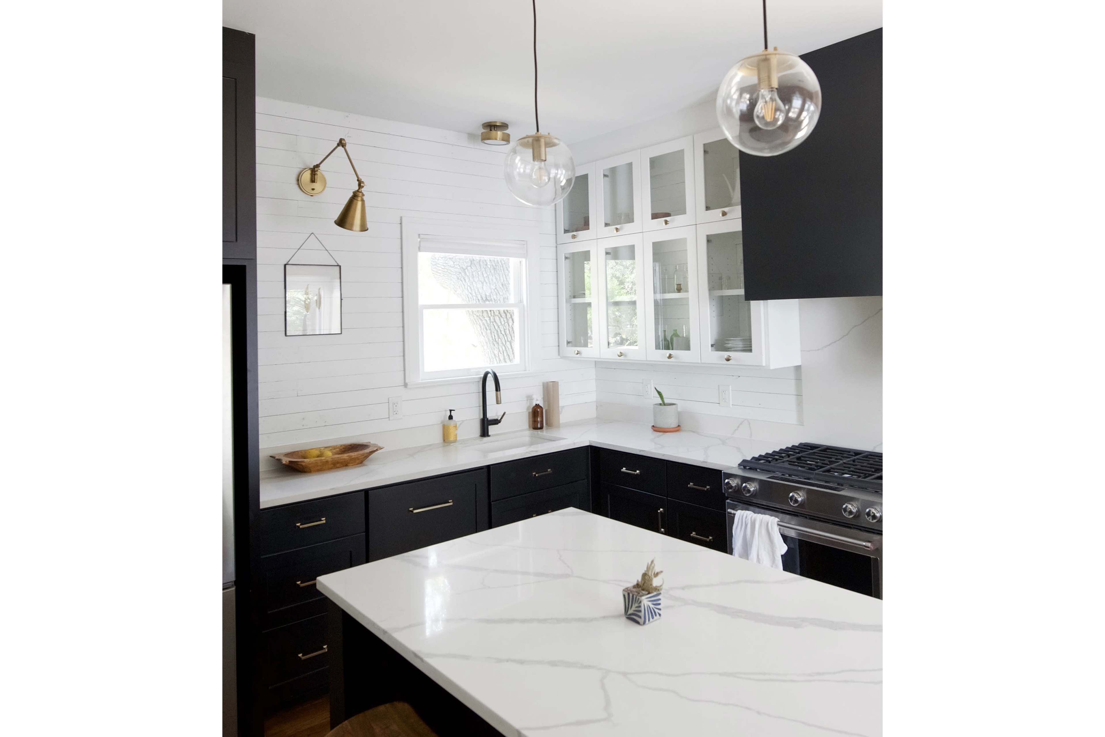 A modern kitchen with black cabinetry, a large white marble island, and two pendant lights hanging from the ceiling.