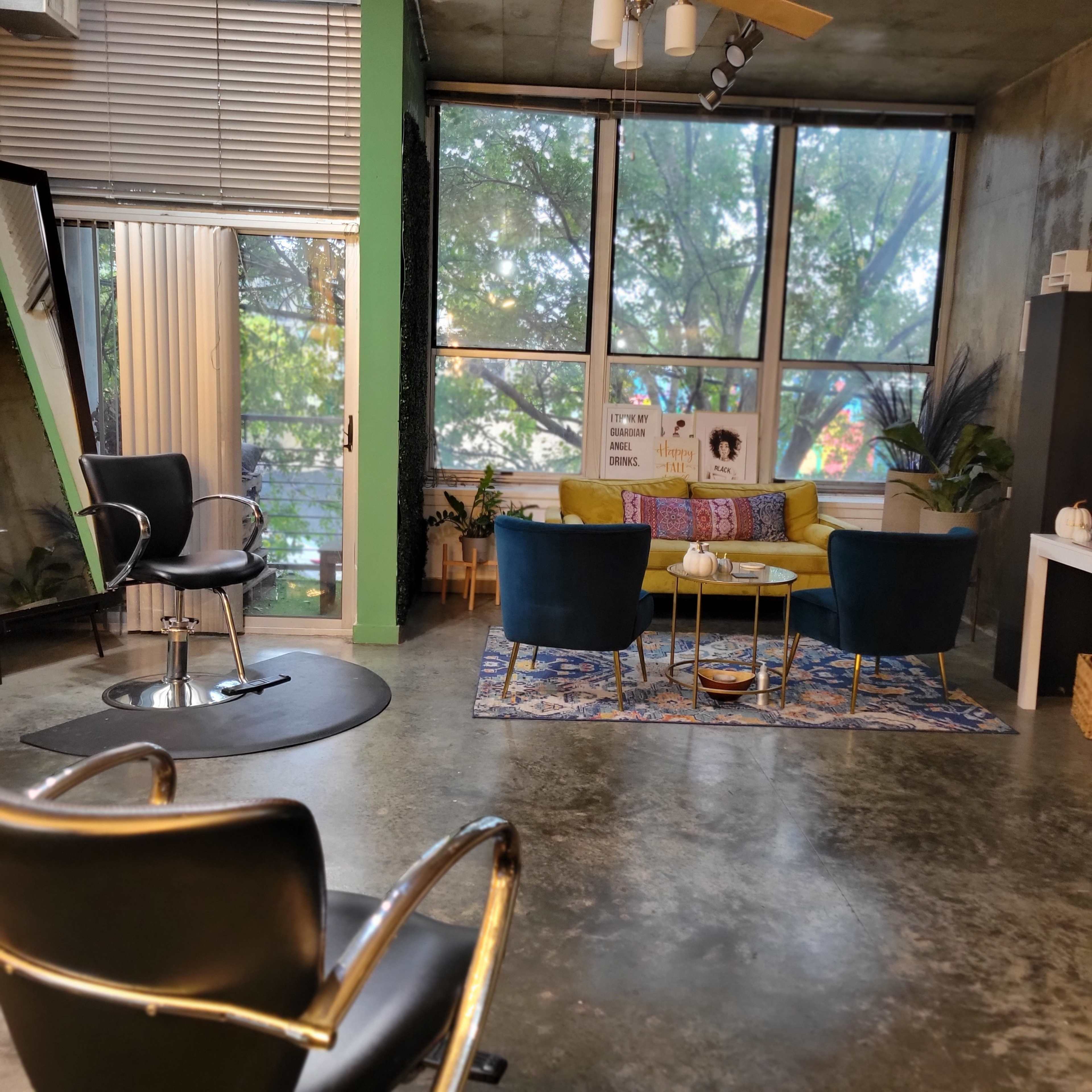 A modern interior space featuring a circular area with a salon chair, a seating arrangement of colorful couches, and large windows allowing natural light to illuminate the room.