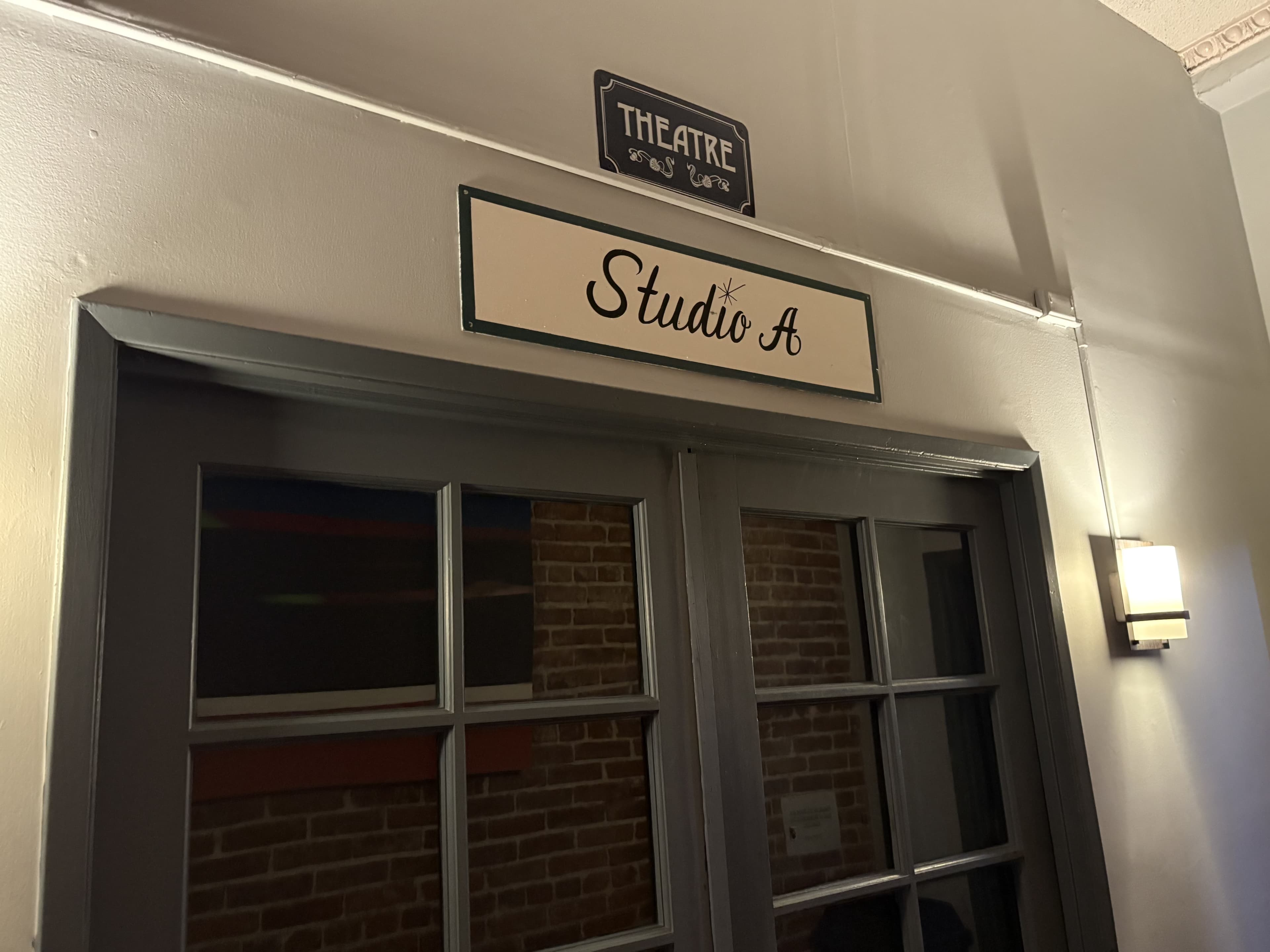 The image shows a door with a sign labeled "Studio A" located below a "Theatre" sign in a well-lit hallway.