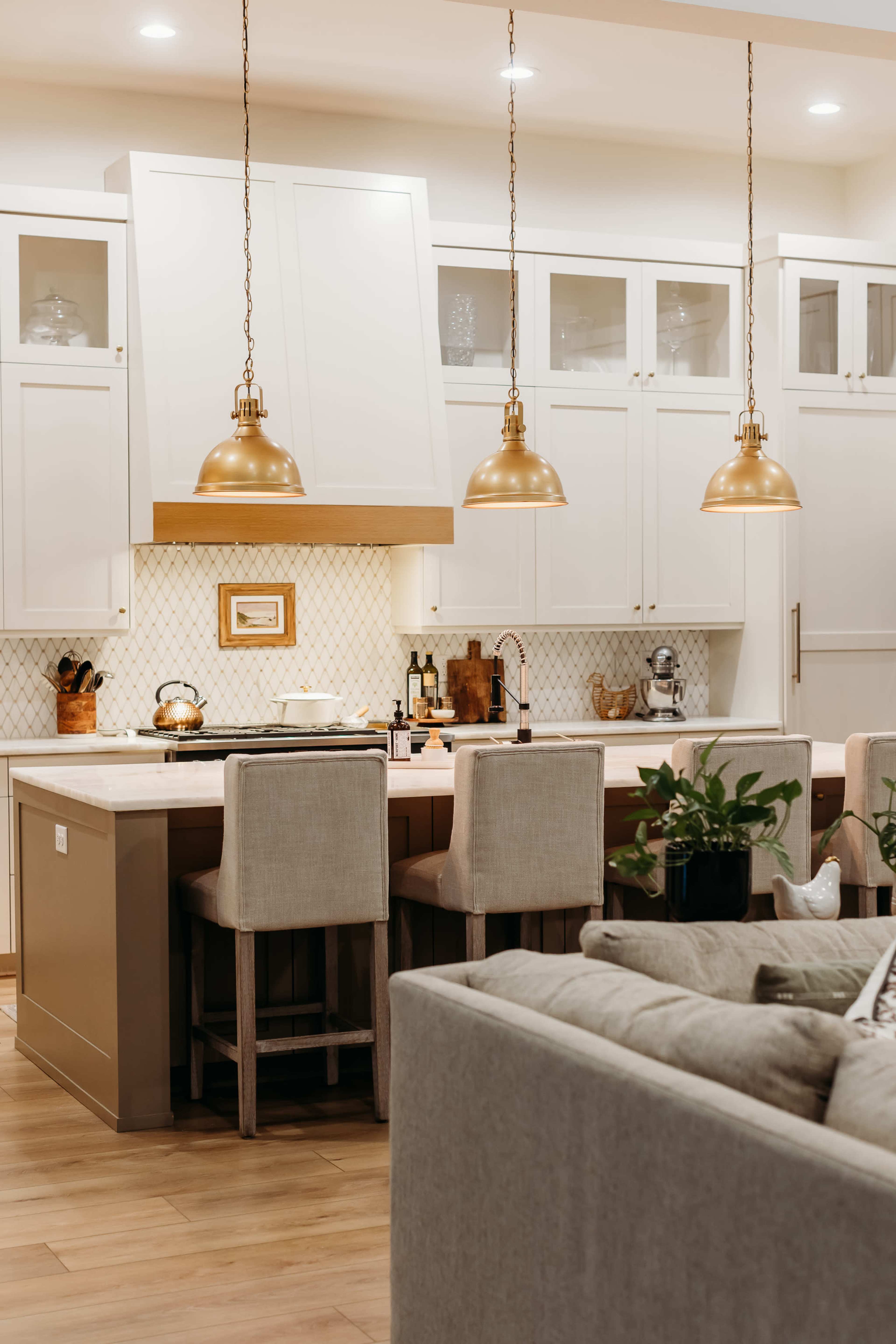 The image shows a modern kitchen with white cabinets, gold pendant lights, and bar seating around an island.