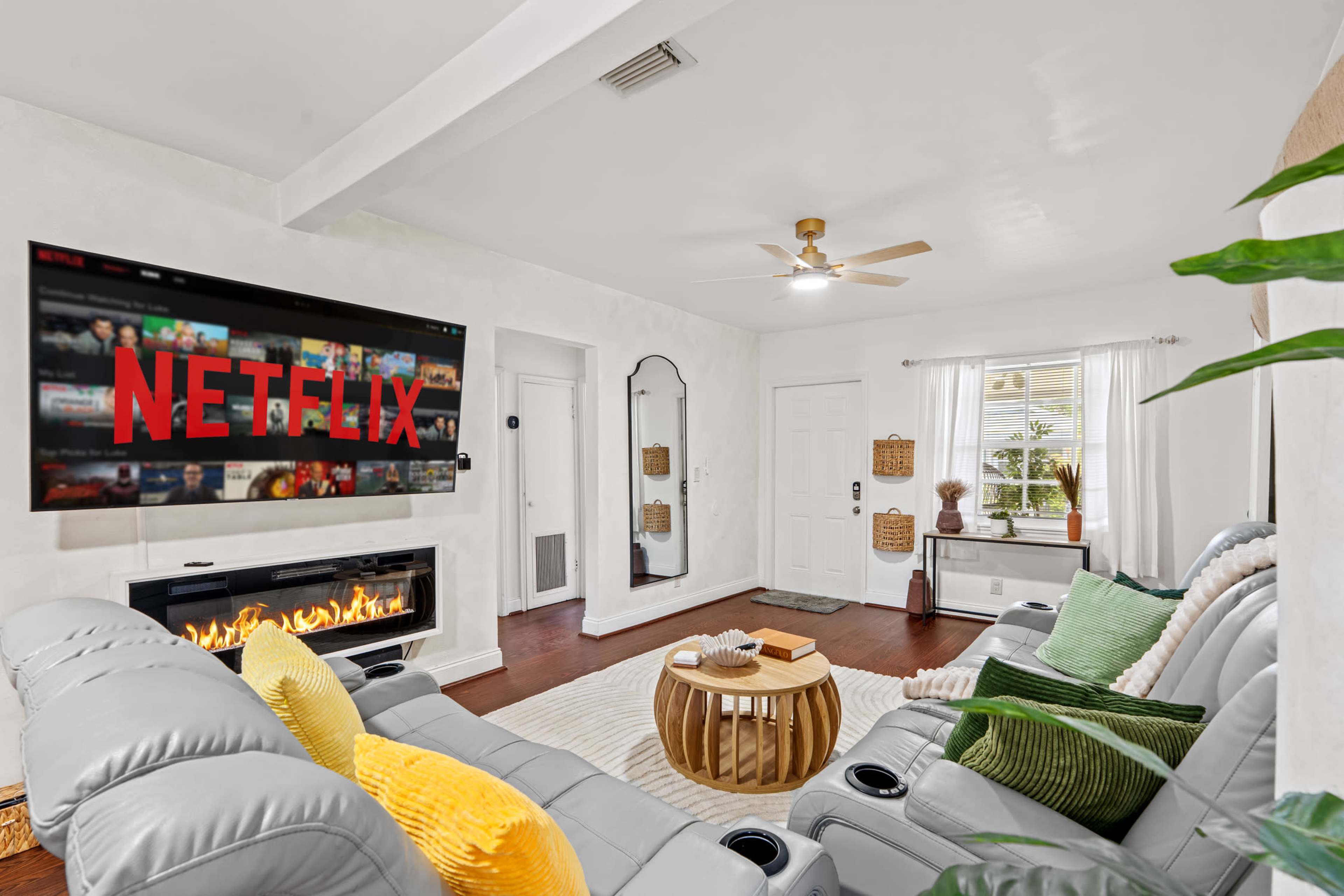 A cozy living room features a large television displaying the Netflix logo, a modern seating area, and natural light streaming through a window.