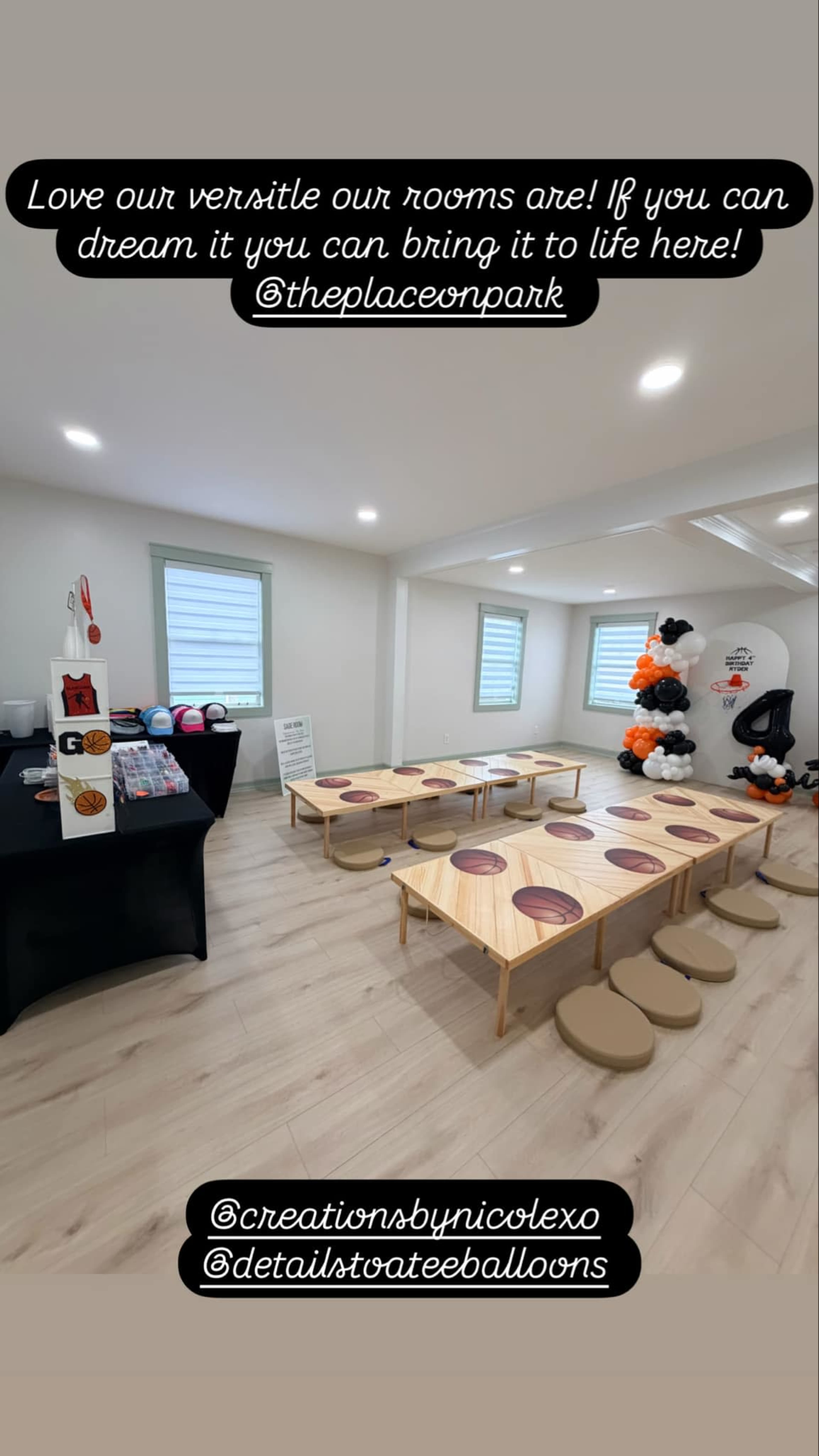 The image shows an indoor event space set up with wooden tables and circular cushions, decorated with balloons and a display table in the corner.