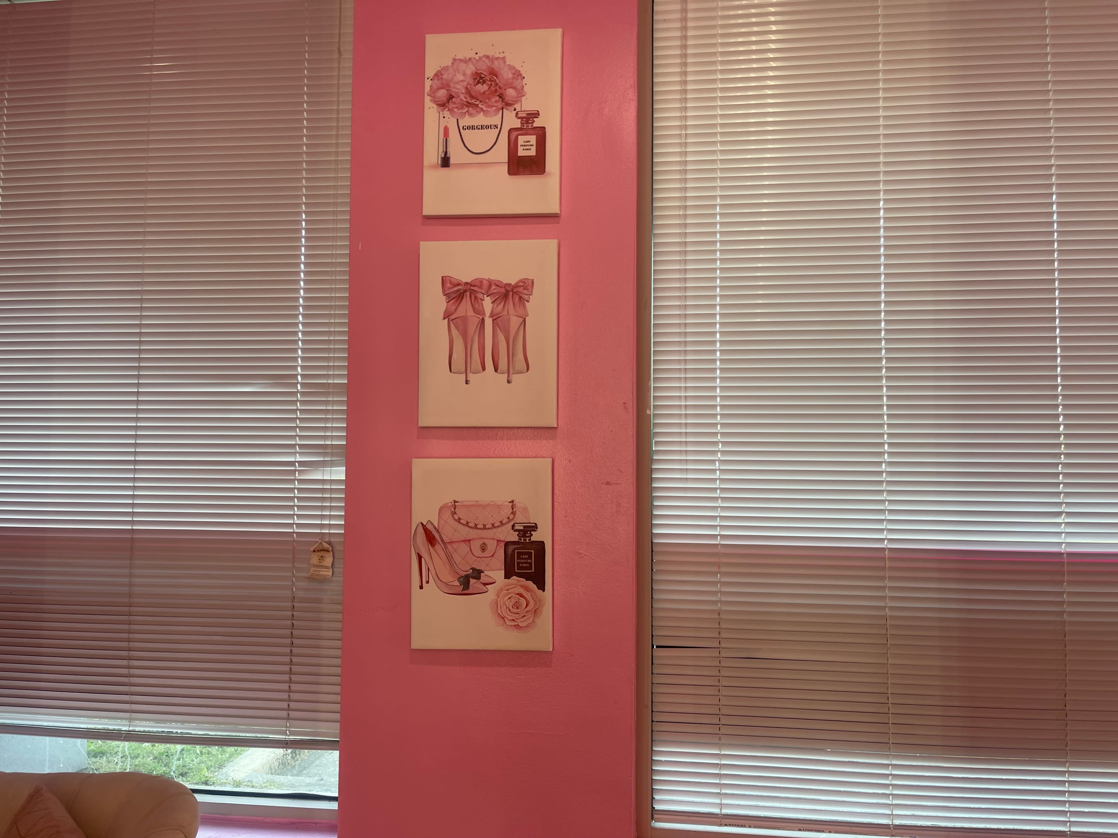 Three framed decorative illustrations on a pink wall, depicting a floral arrangement, a pair of stockings with bows, and a vintage handbag adorned with a rose.