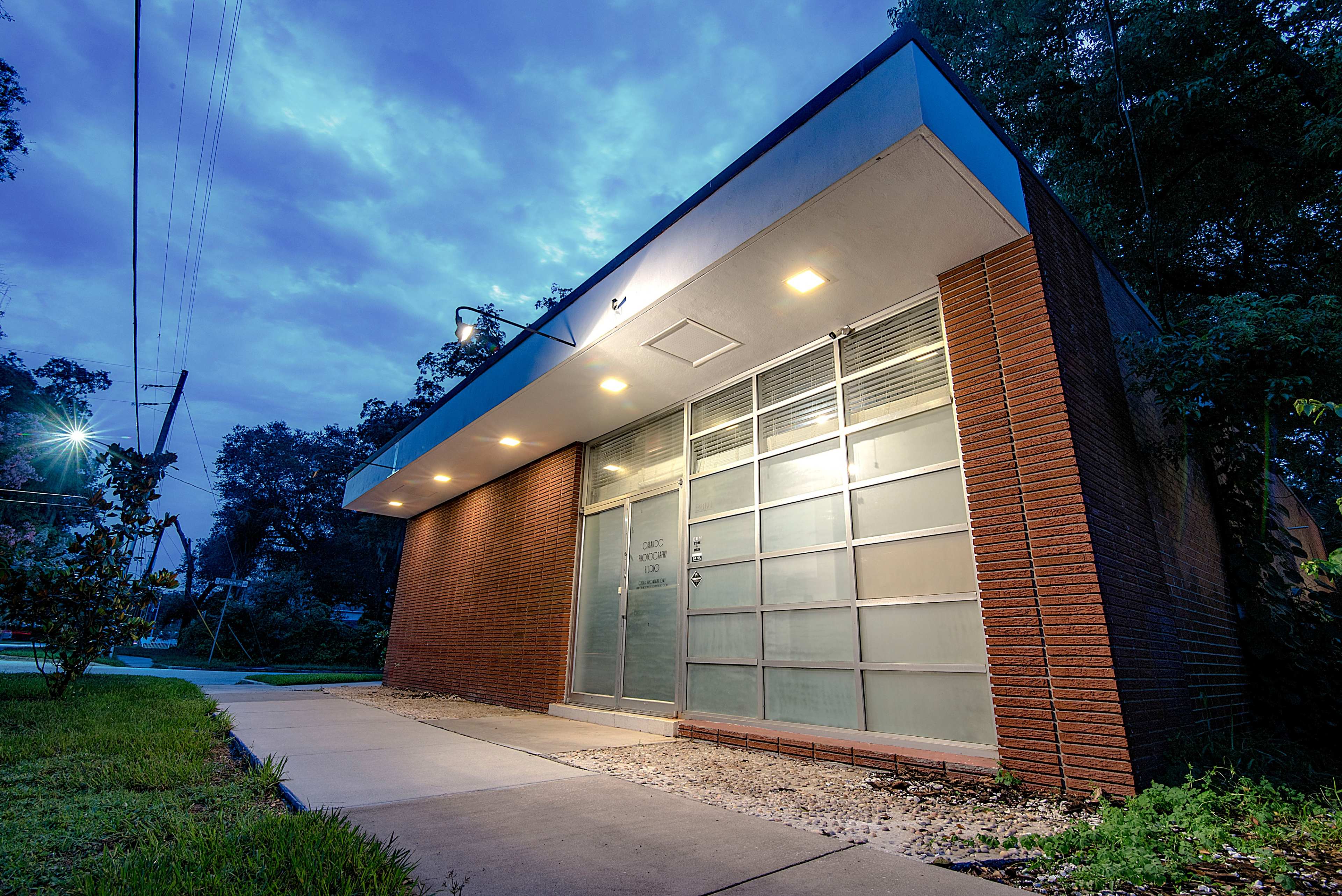 A small, modern brick building with large glass windows is illuminated under an evening sky.