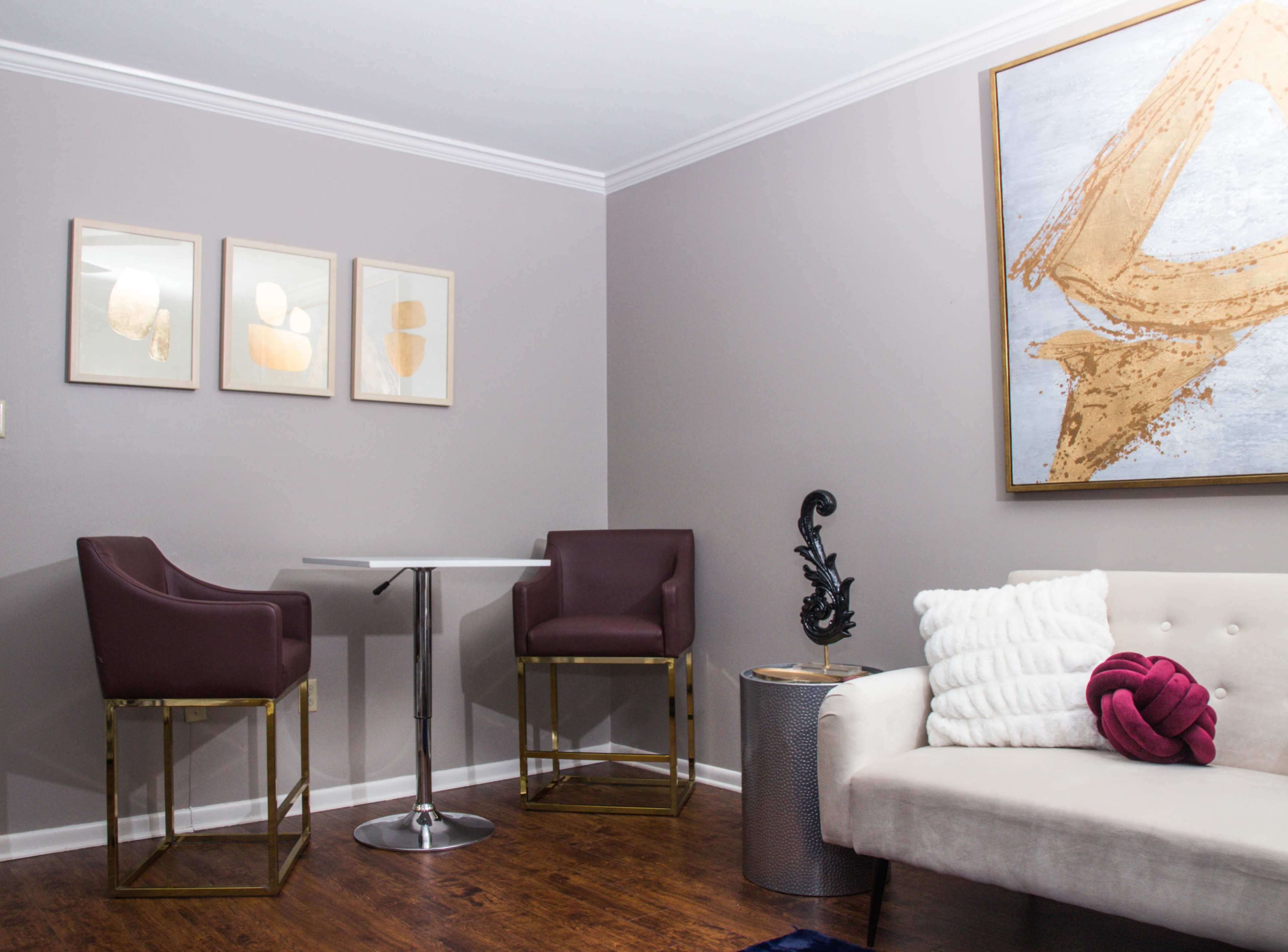 A modern sitting area features a light-colored sofa, two high-backed chairs at a round table, and framed artwork on the walls.