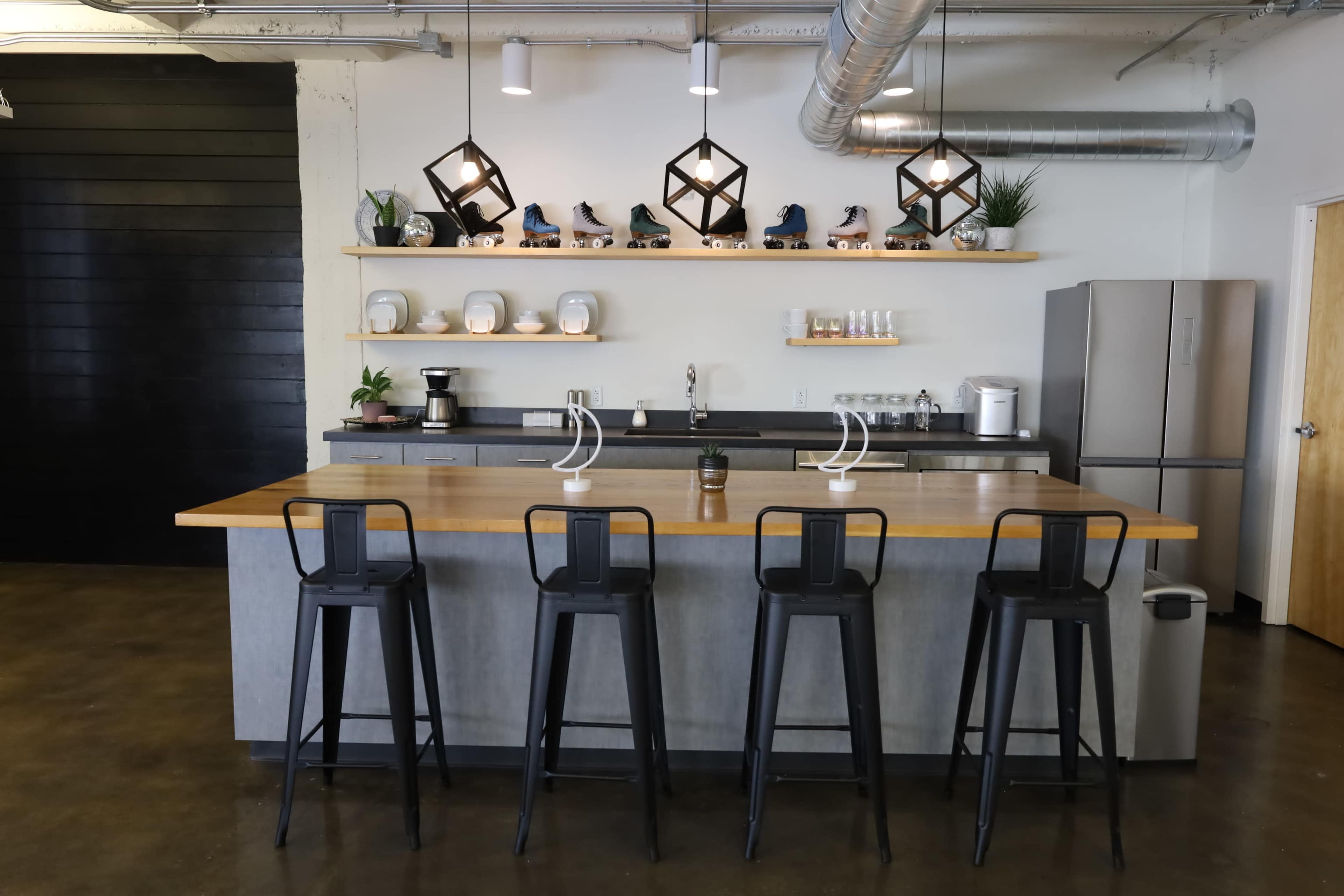 A modern kitchen features a gray island with bar stools, shelves displaying decorative items and roller skates, and a stainless steel refrigerator.