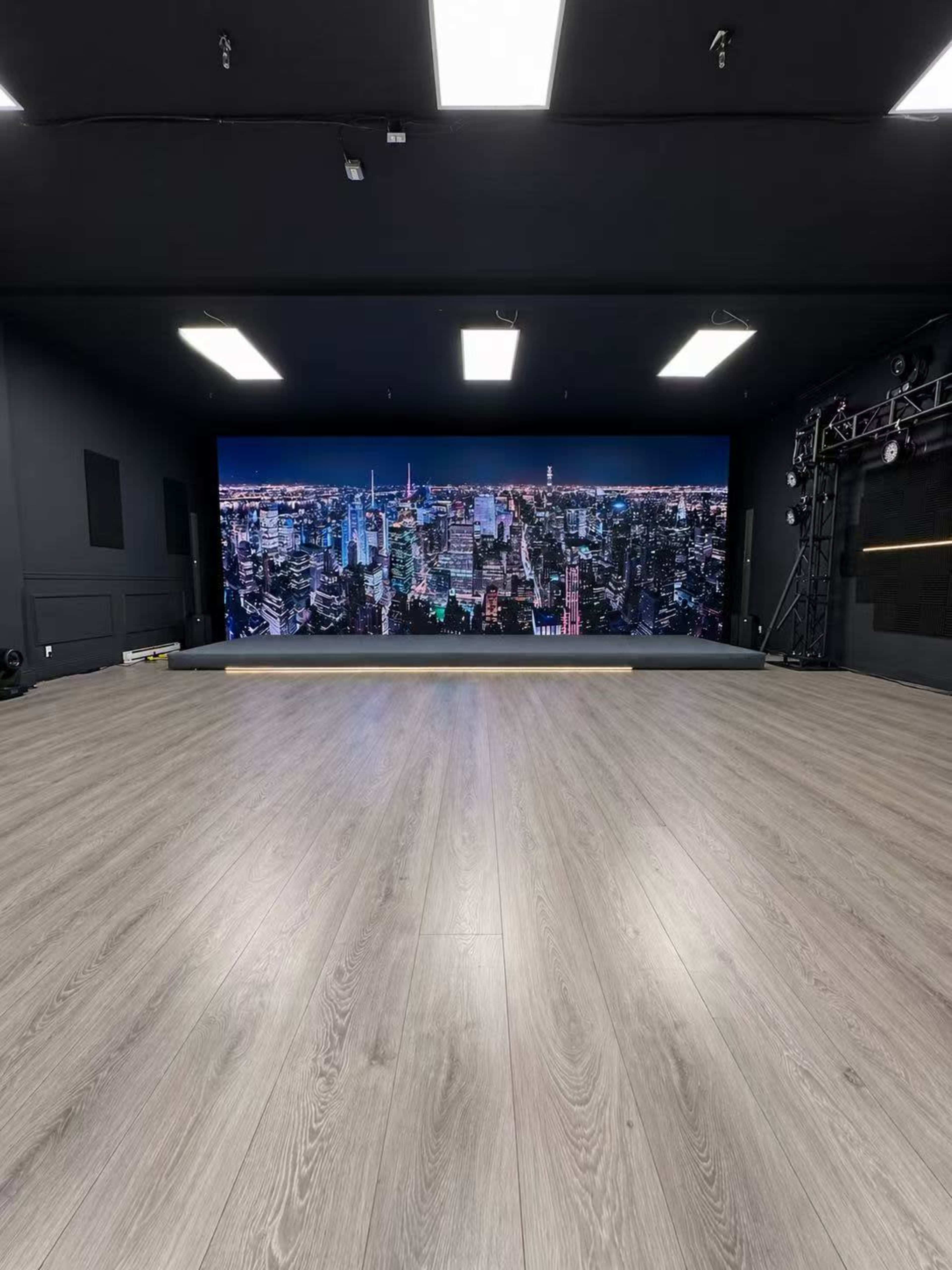 The image shows an indoor studio space with a large backdrop of a city skyline and light wooden flooring.