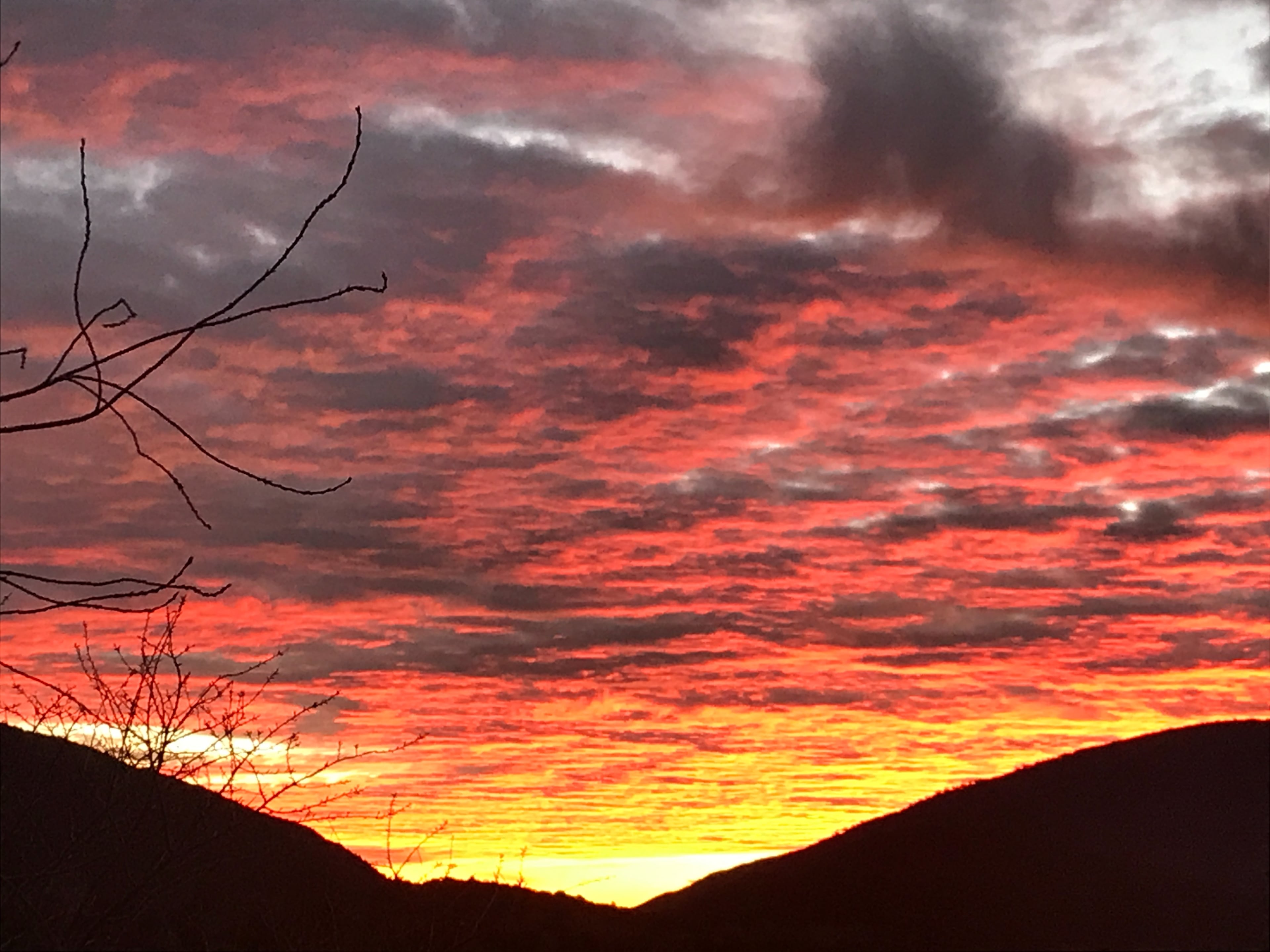 A vibrant sunset casts orange and red hues across the sky, silhouetting the hills in the foreground.