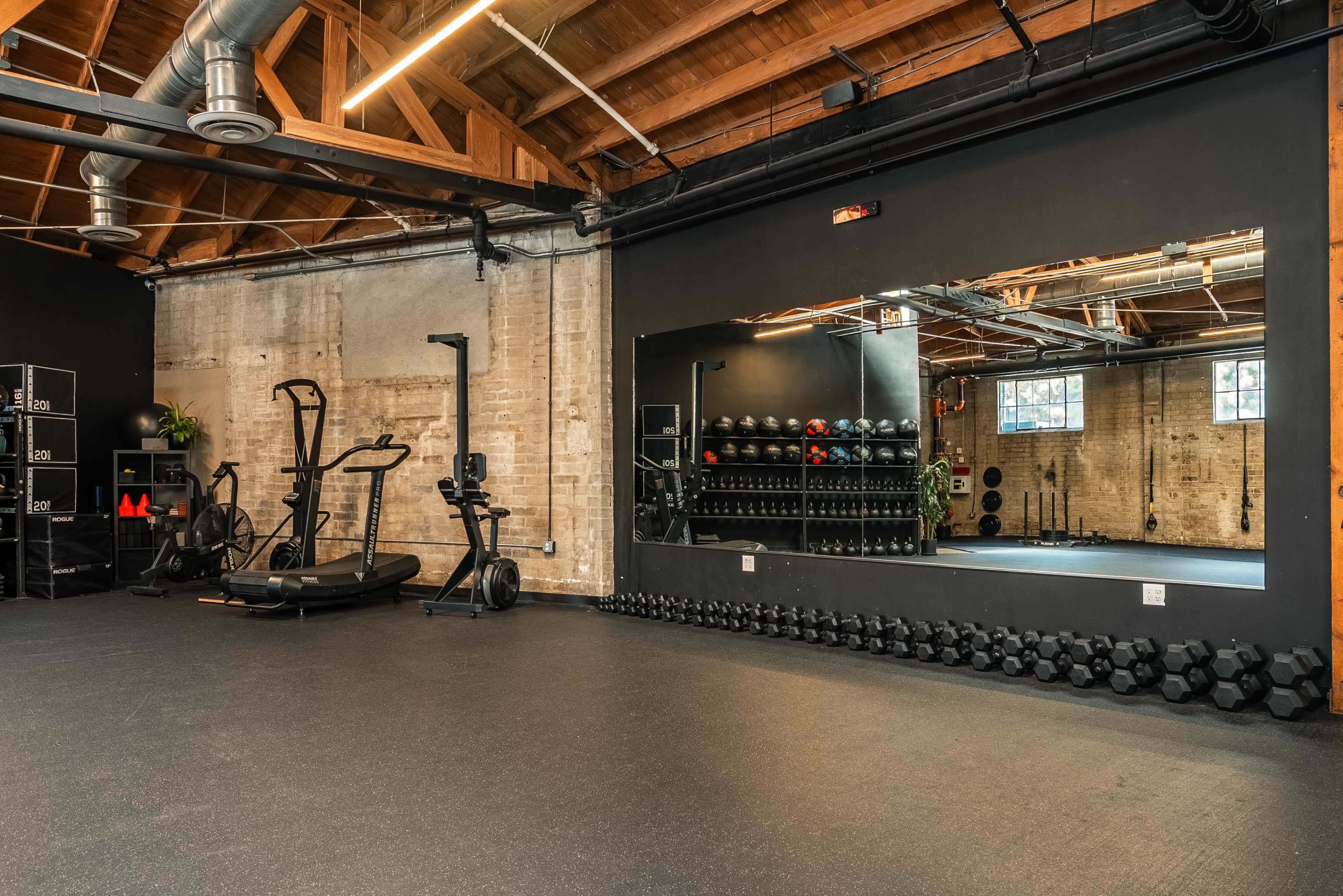 The image shows a modern gym interior with exercise equipment including a treadmill, kettlebells, and dumbbells arranged neatly along the wall.