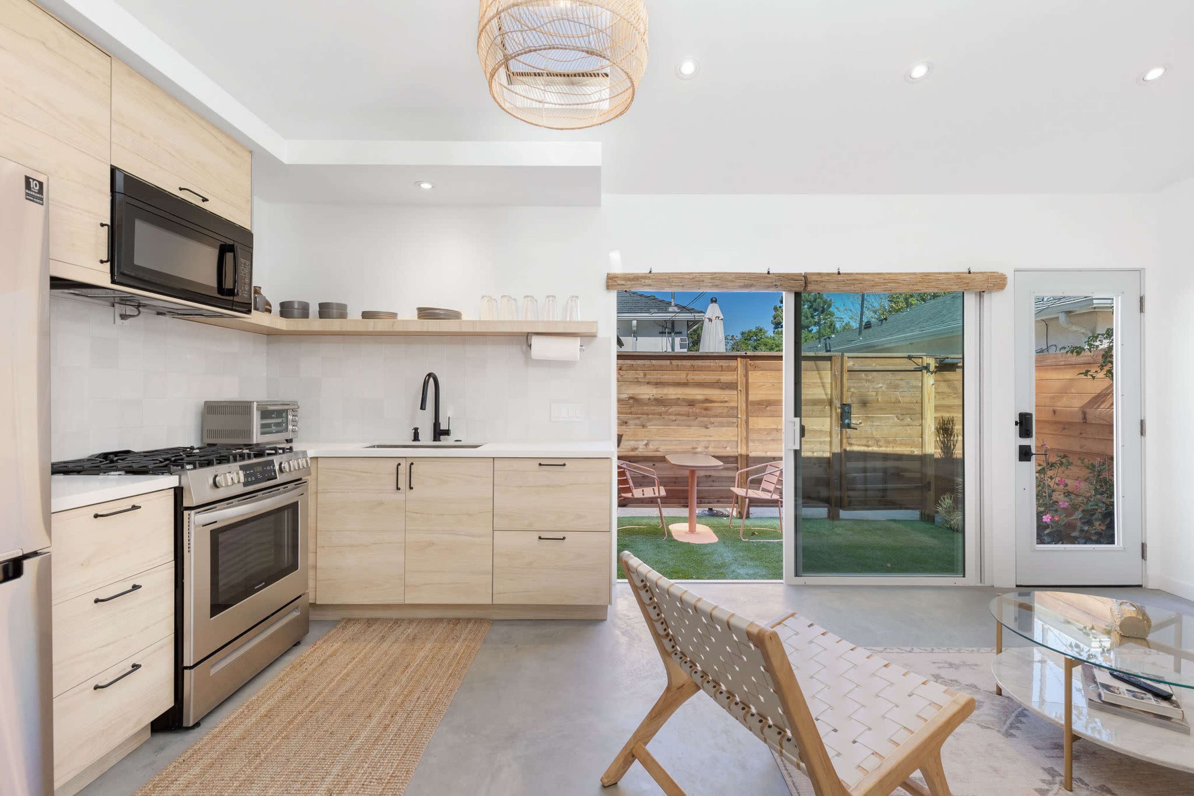 A modern kitchen featuring light wood cabinets, stainless steel appliances, and a sliding glass door leading to a backyard patio.