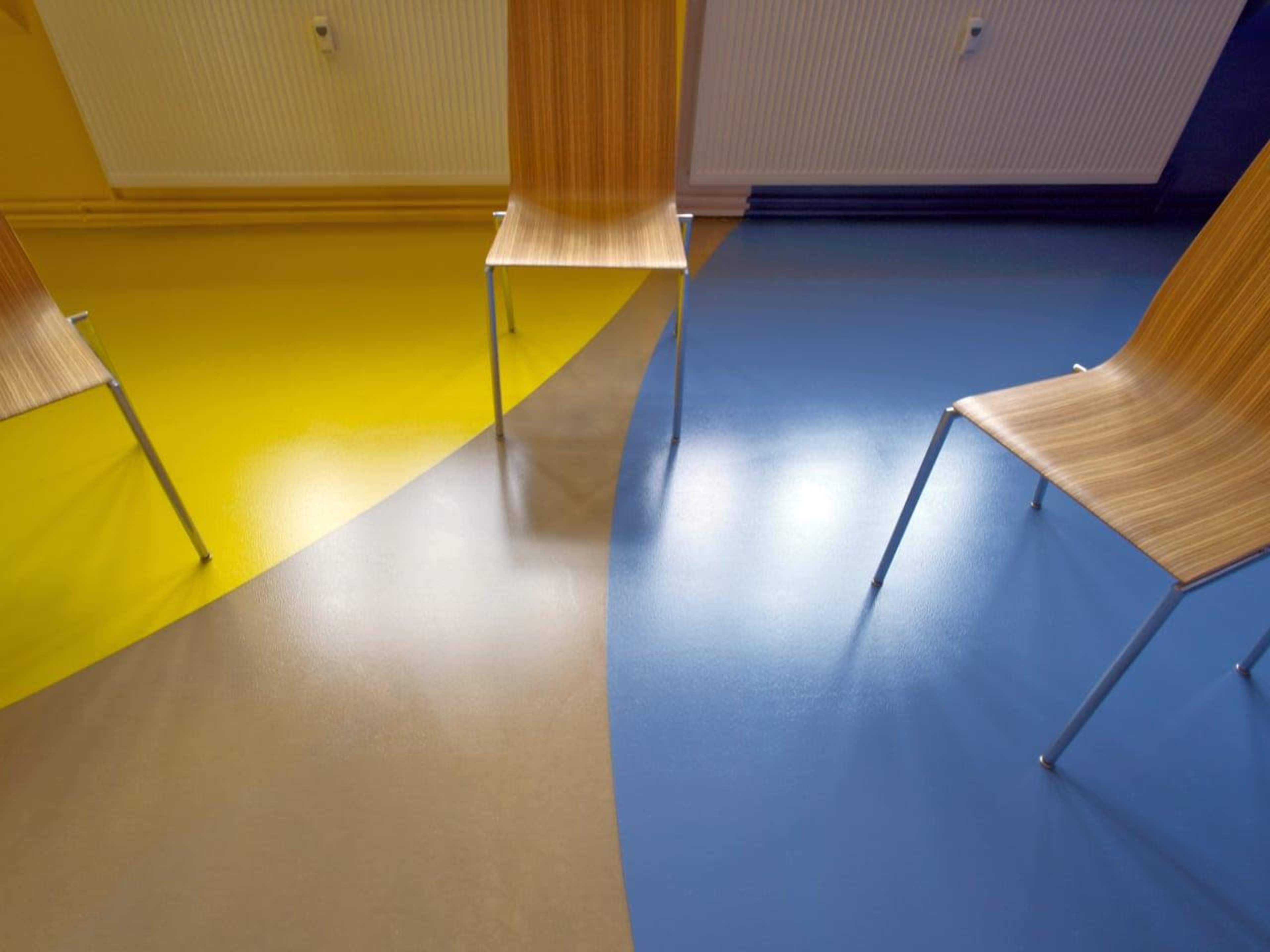 The image shows three wooden chairs positioned on a floor with distinct sections of yellow, gray, and blue colors.