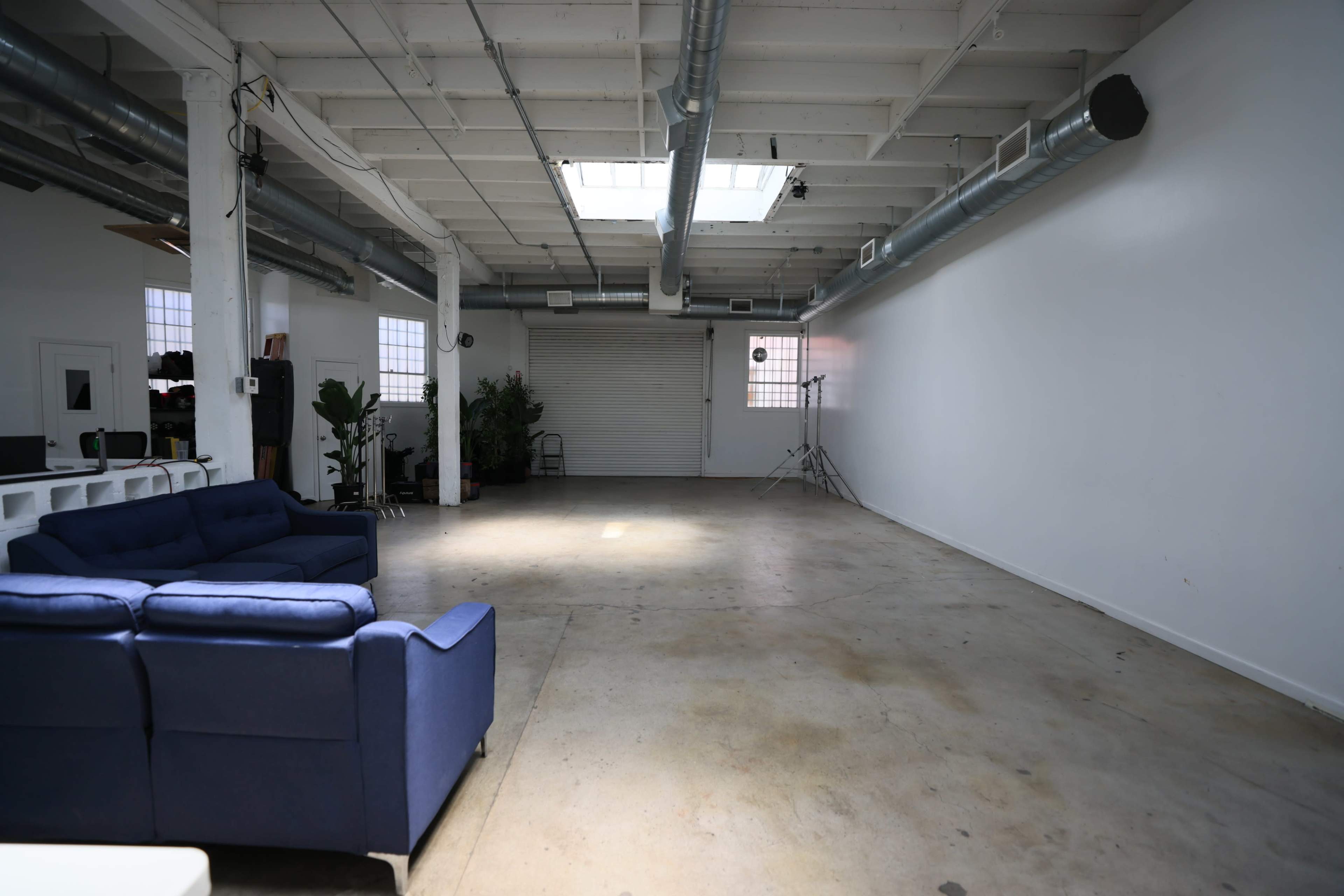 A spacious, empty interior with a blue sofa on one side and large windows providing natural light.