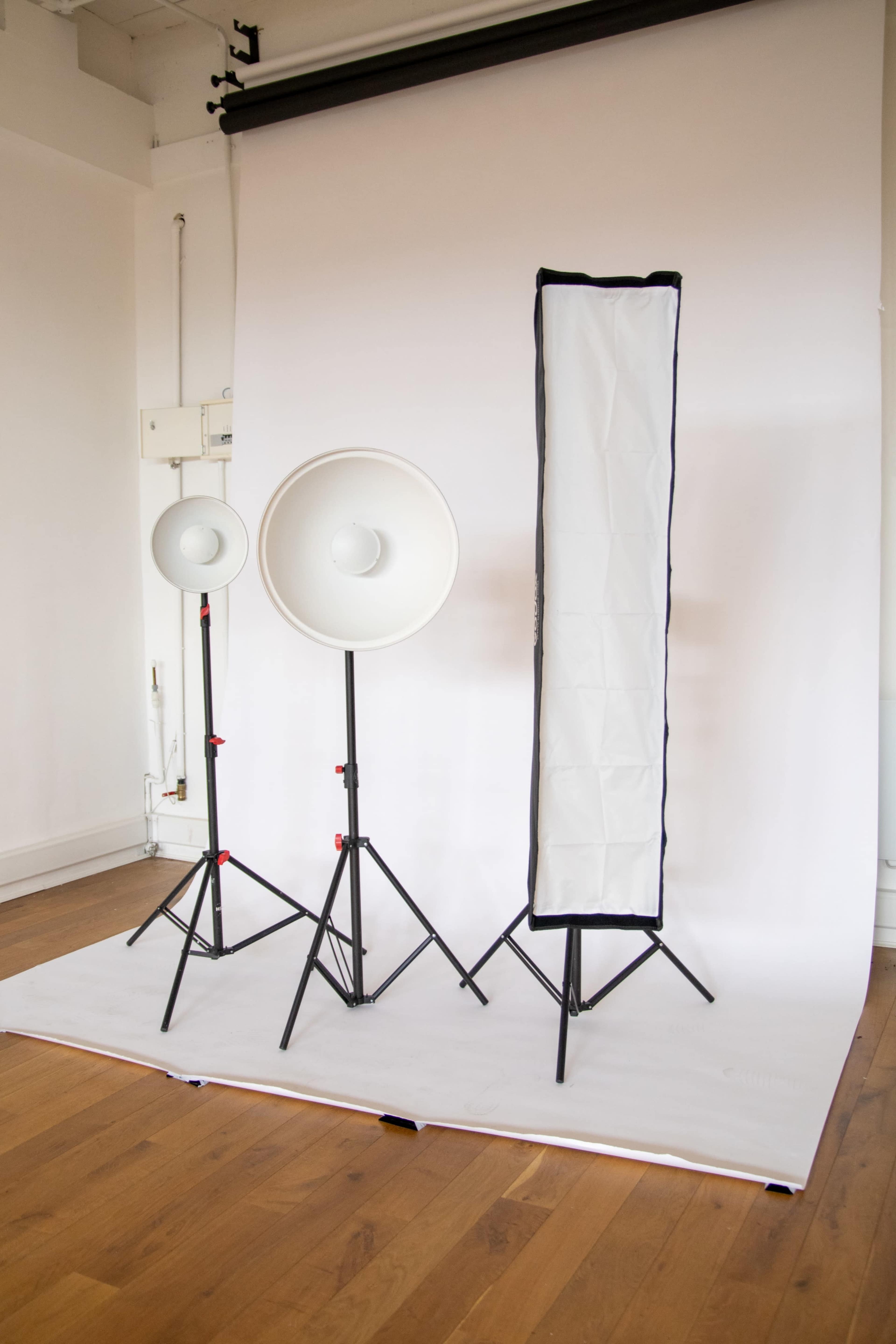 Two light stands with round softboxes and a tall, narrow softbox are set up against a plain backdrop in a photography studio.