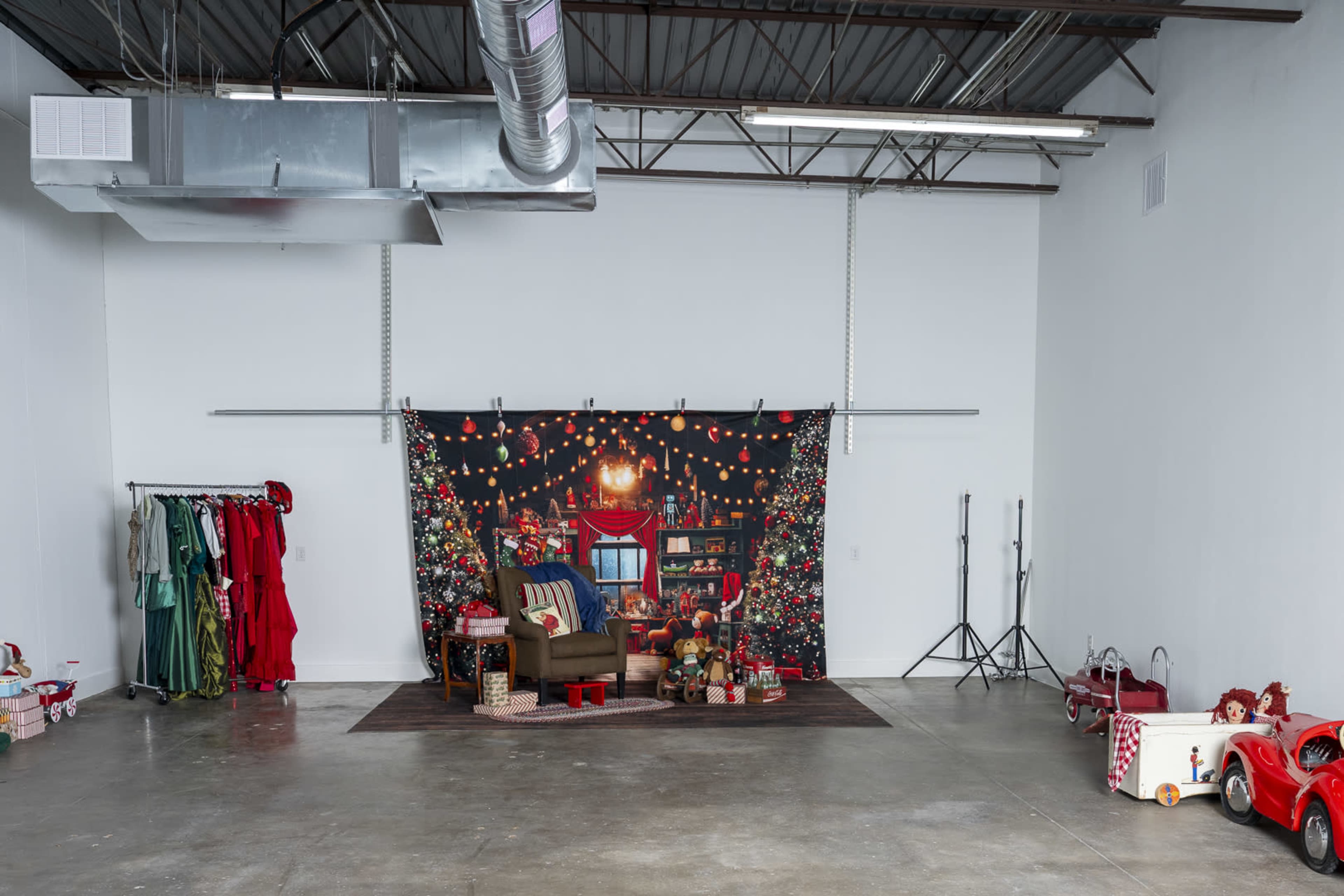 The image shows a spacious studio with a decorated backdrop for a Christmas scene, featuring a chair, festive lights, and various holiday decorations, along with colorful costumes and props along the walls.