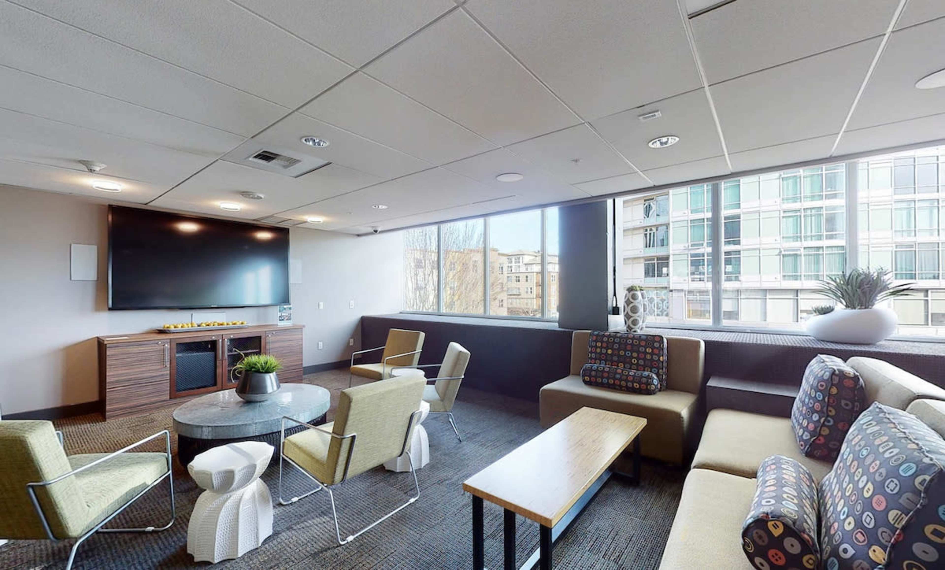 A modern lounge area with seating, a large television, and windows providing natural light.