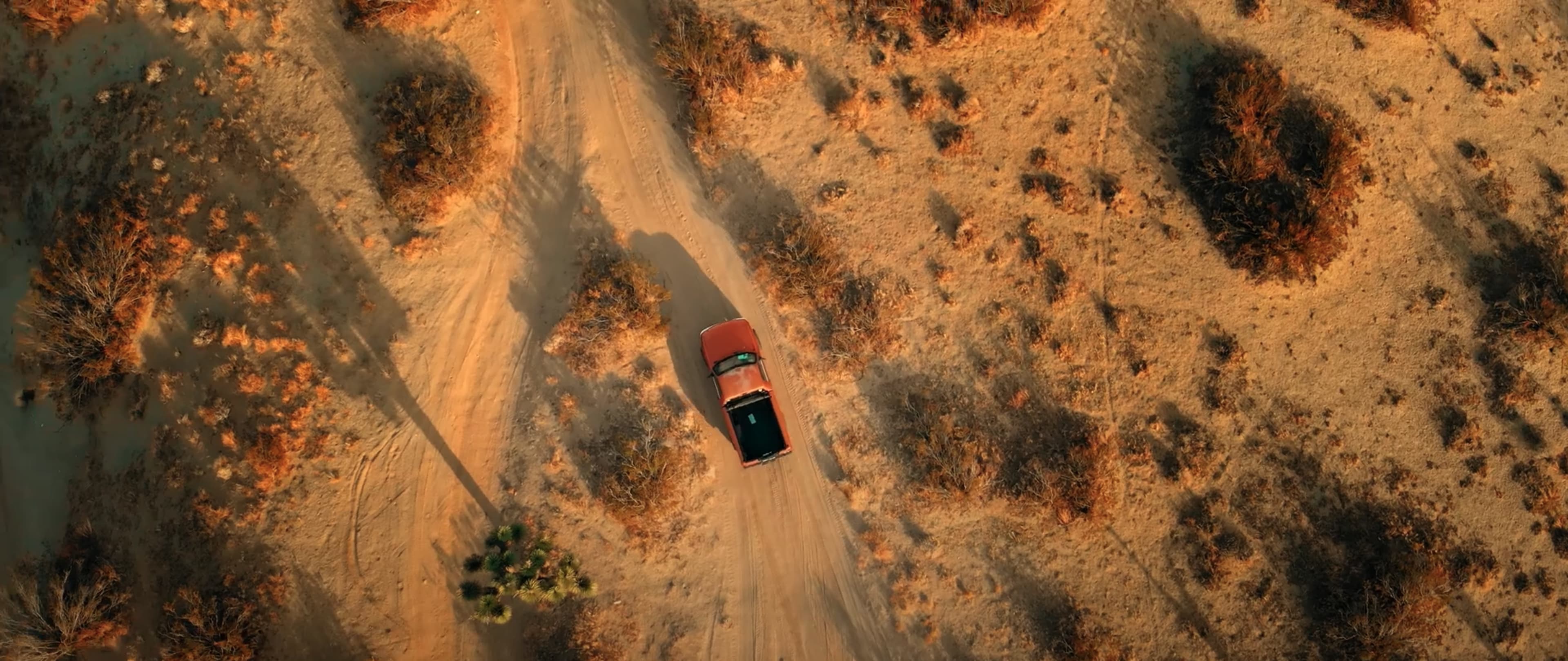 A red car drives along a winding dirt road surrounded by sparse vegetation and rugged terrain.