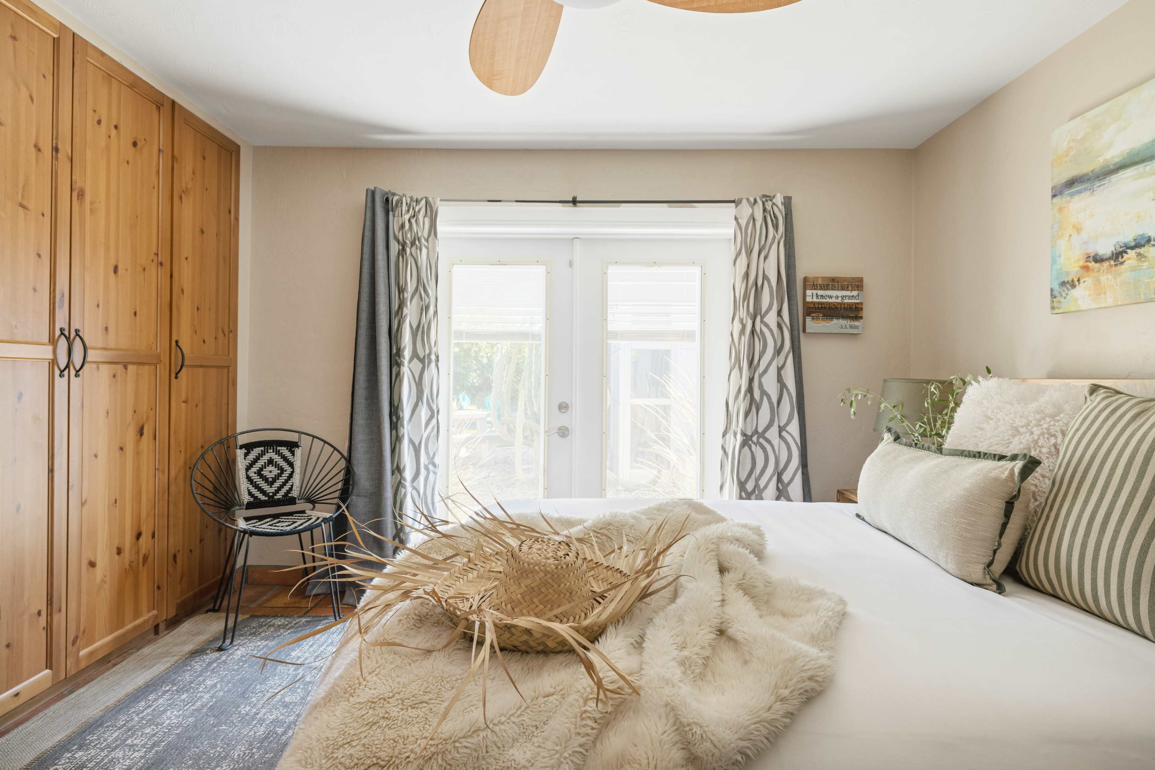 The bedroom features a bed with a textured throw, a chair, a wooden wardrobe, and doors leading to an outdoor space.