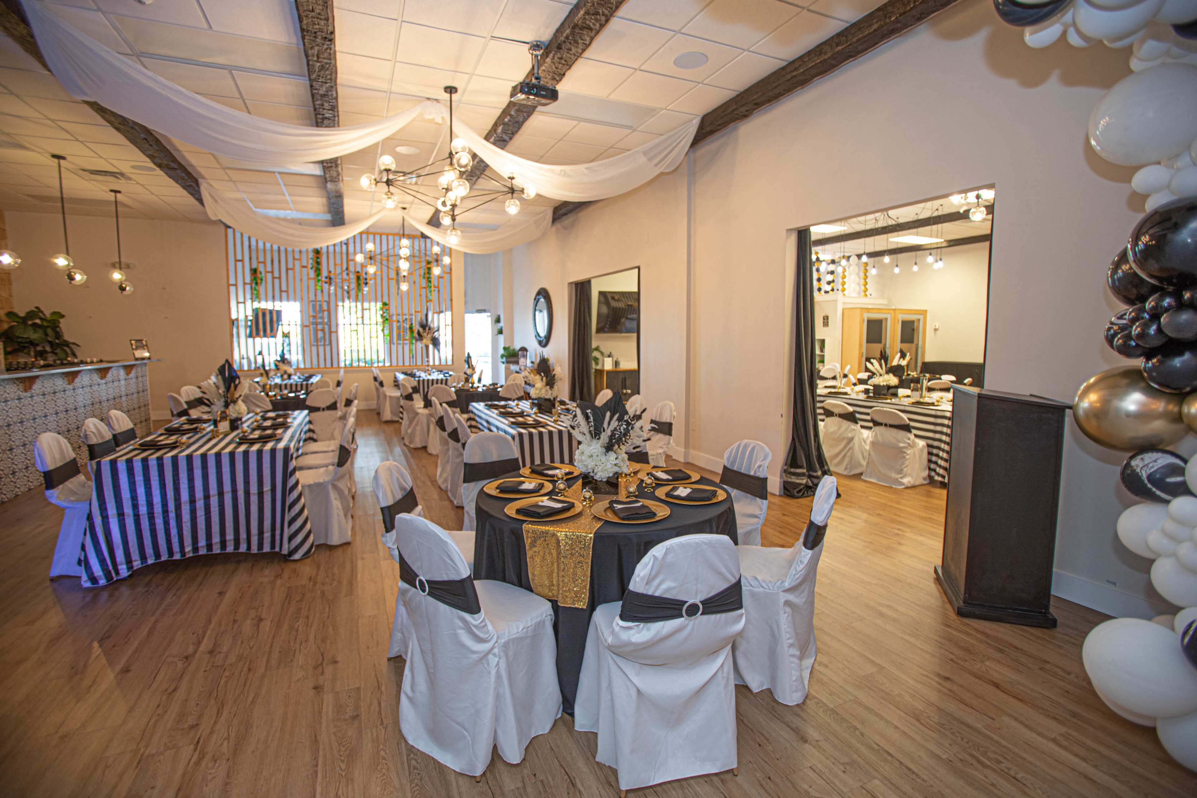 A banquet hall set up with tables covered in black and white striped and solid tablecloths, decorated with elegant table settings, and stylish balloon arrangements on one side.