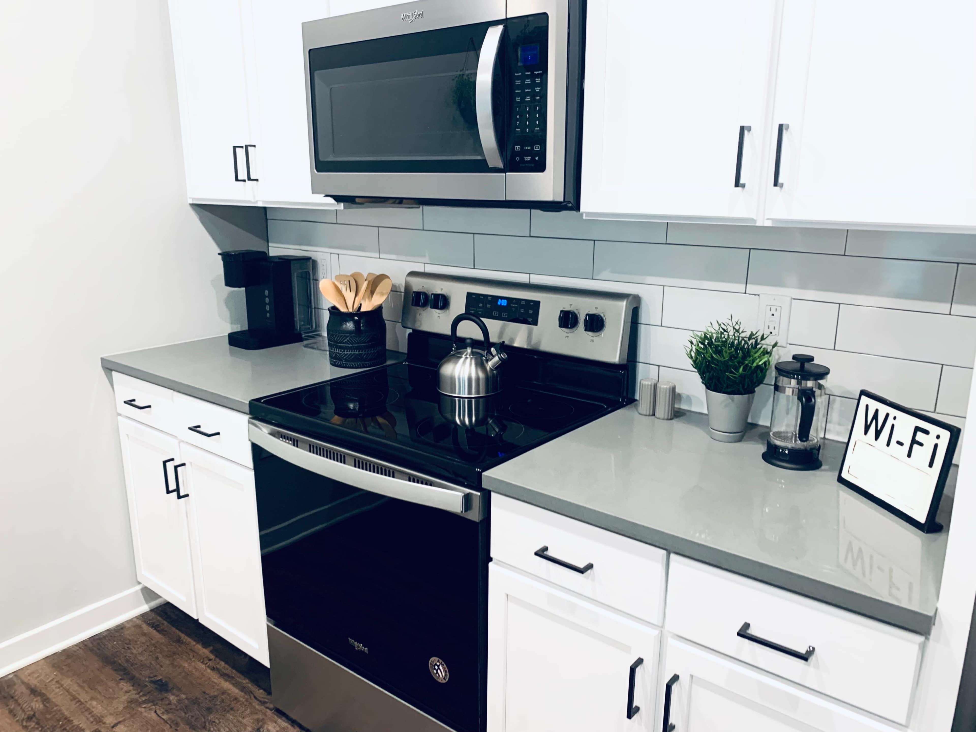 A modern kitchen features a black stove and microwave, white cabinets, a coffee maker, and a small plant on the countertop.