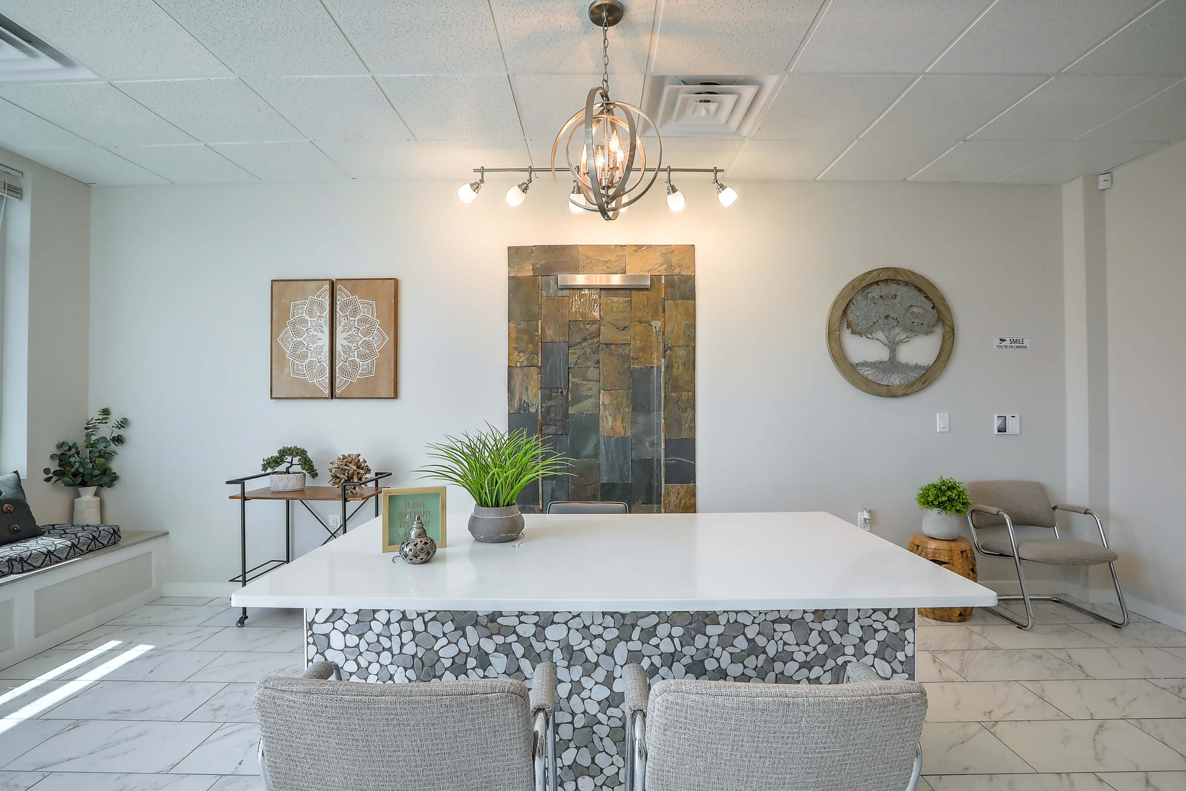 The image shows a modern reception area with a large white table, stone wall art, and minimalist decor.