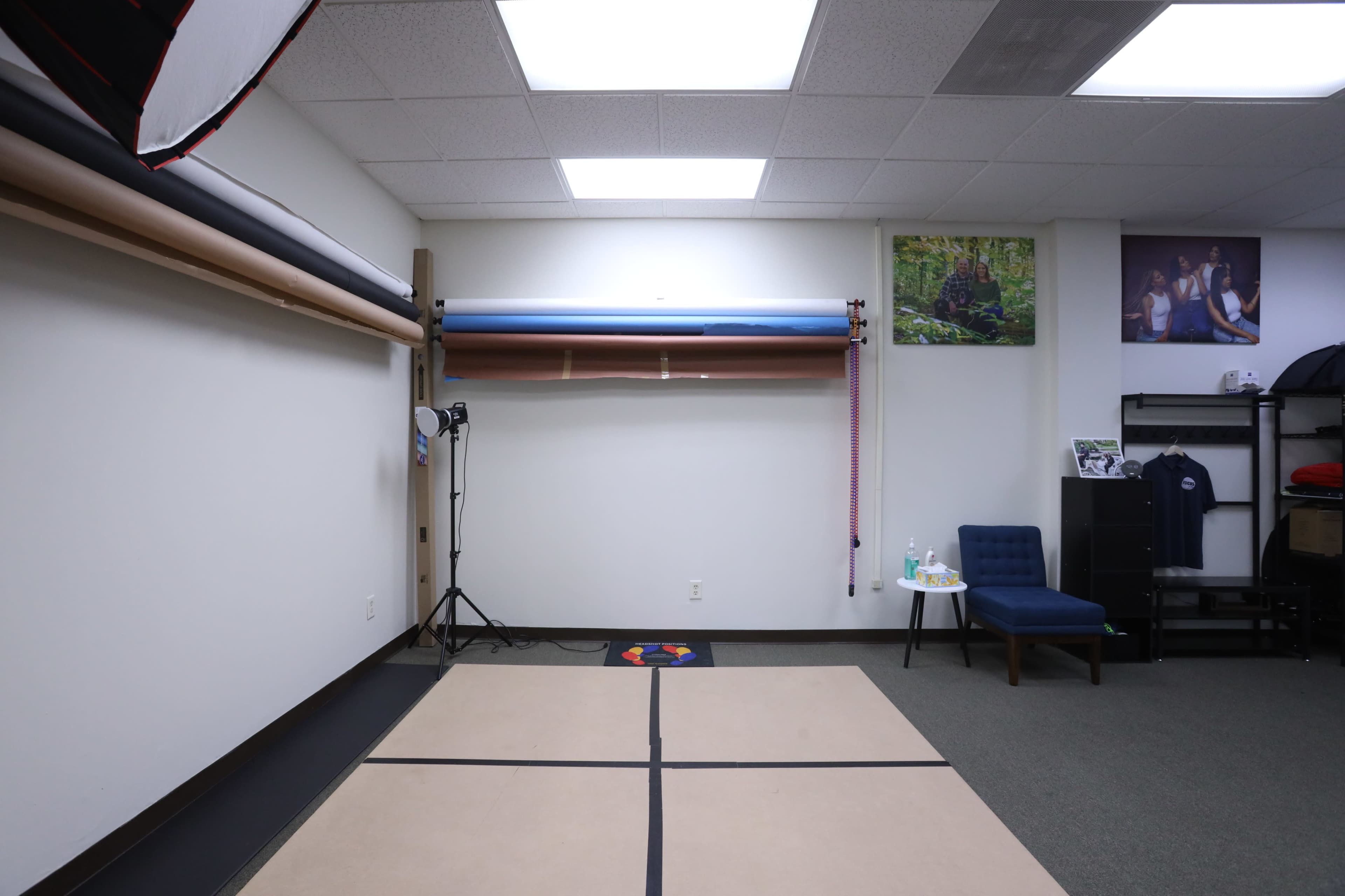 The image shows a sparse room with a beige floor mat arranged in a grid pattern, a blue chair, and two light stands against a white wall.