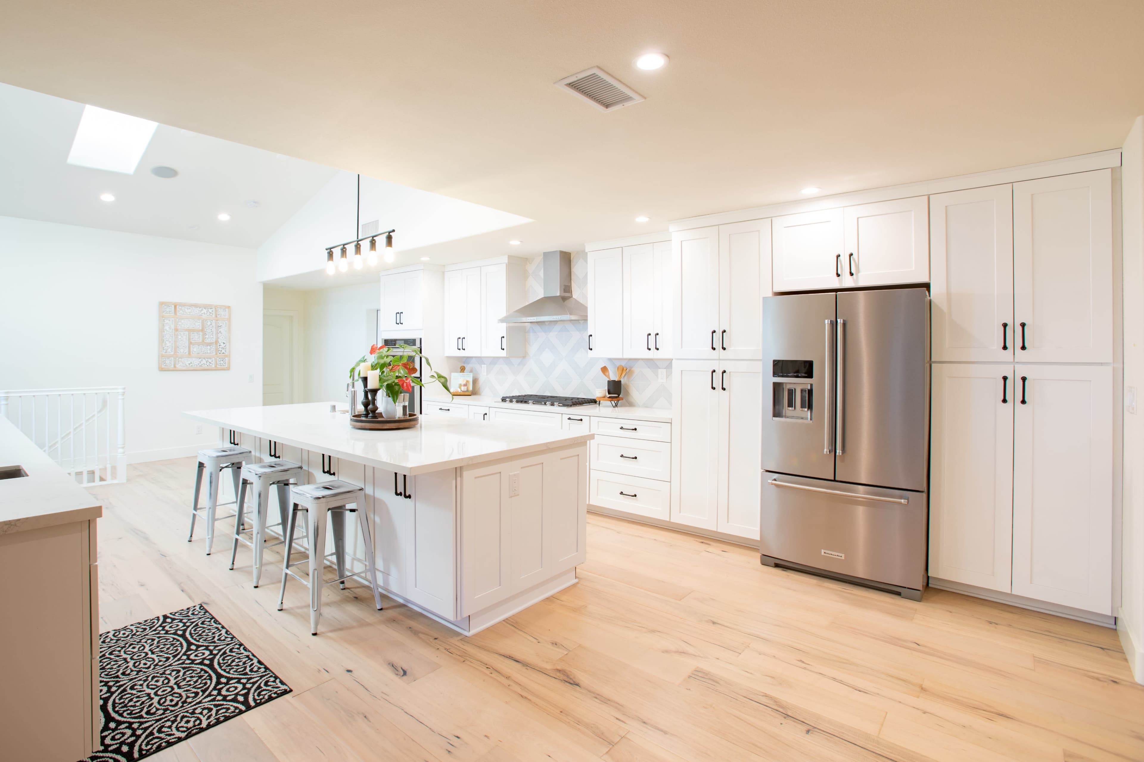 A modern kitchen features white cabinetry, a large central island with bar stools, stainless steel appliances, and hardwood flooring.