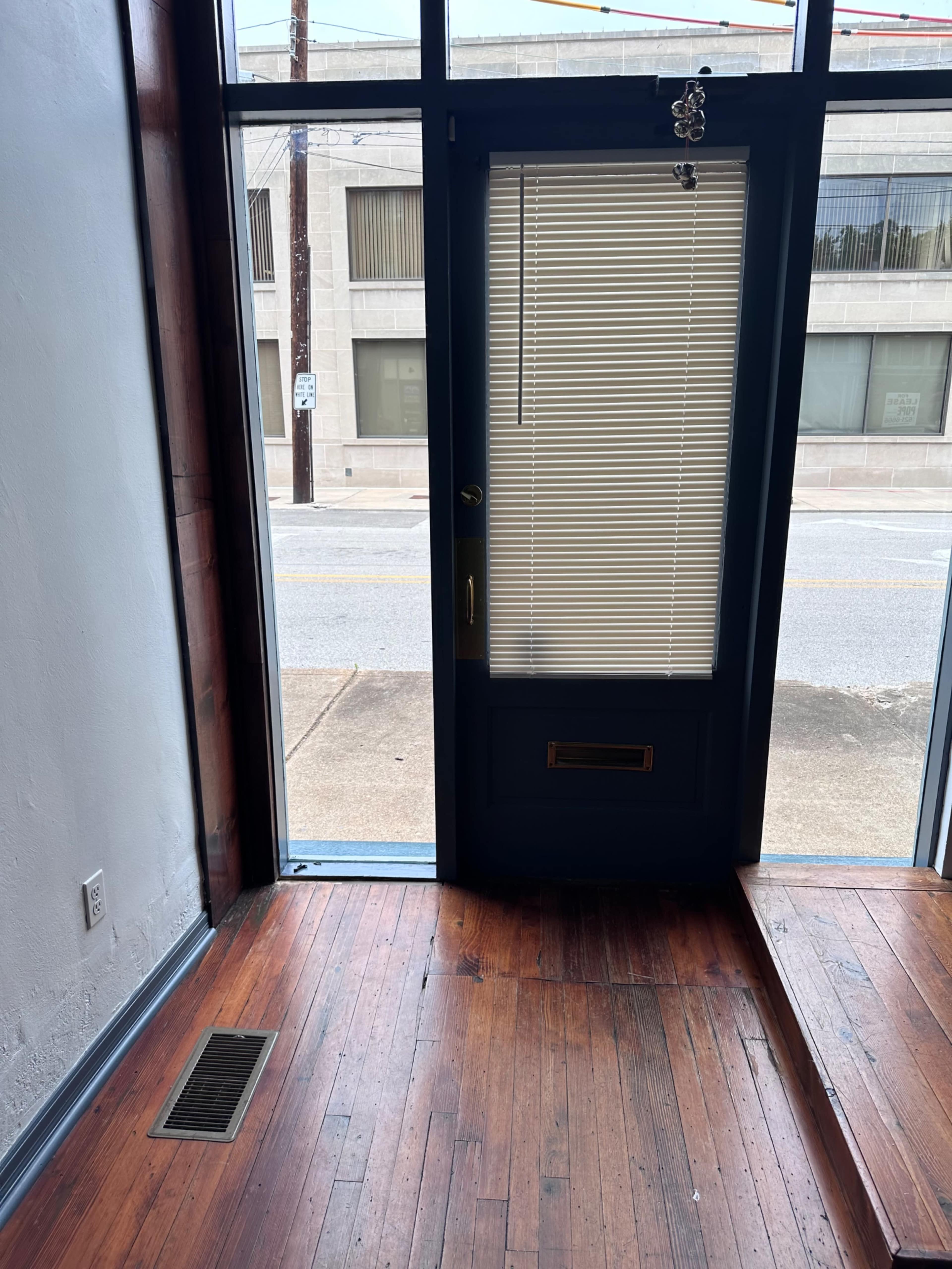 The image shows an interior space with wooden flooring and a door partially open, leading to an outdoor view.