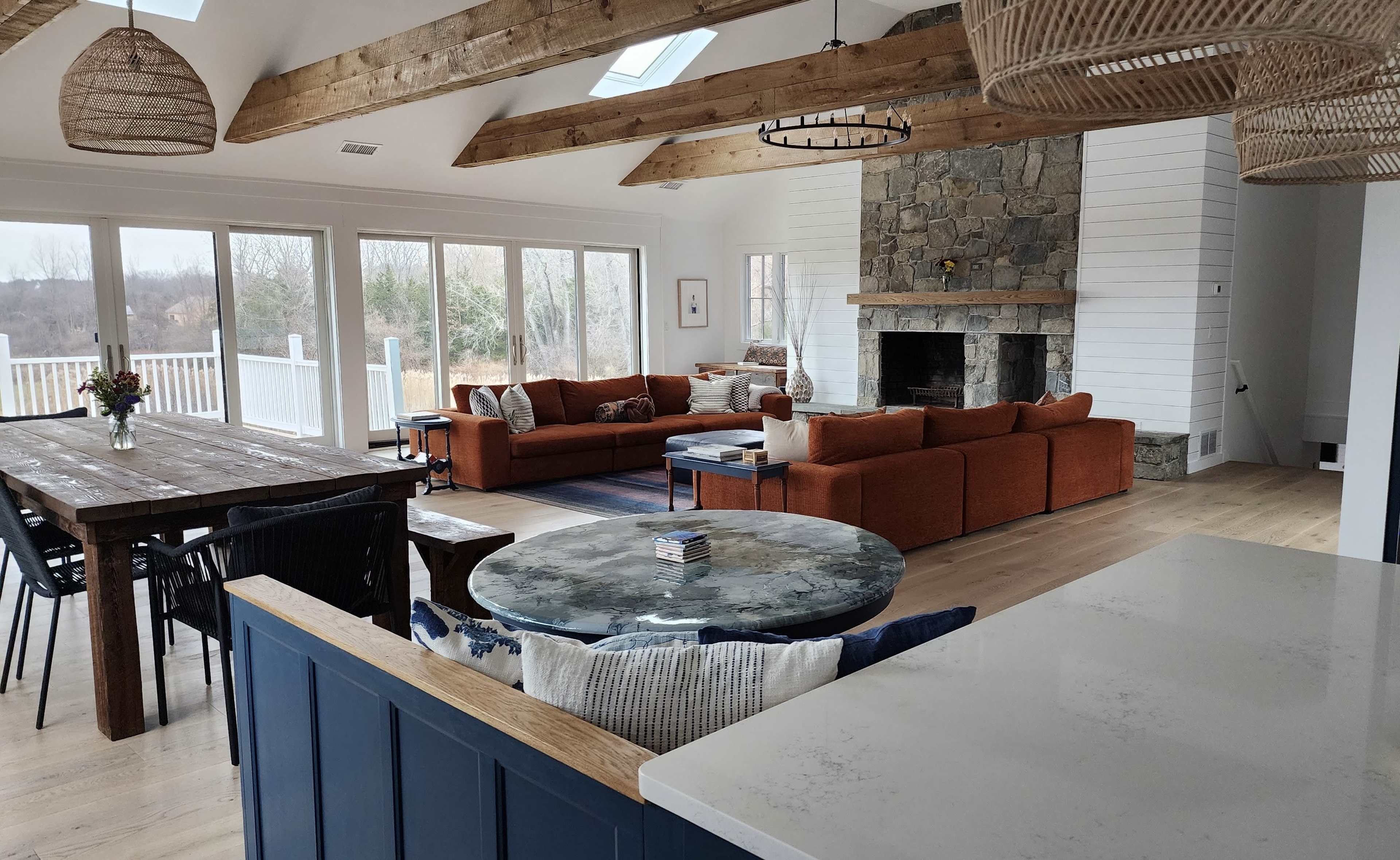 A spacious, modern living area with a stone fireplace, wooden beams, and large windows that offer a view of the outdoors.