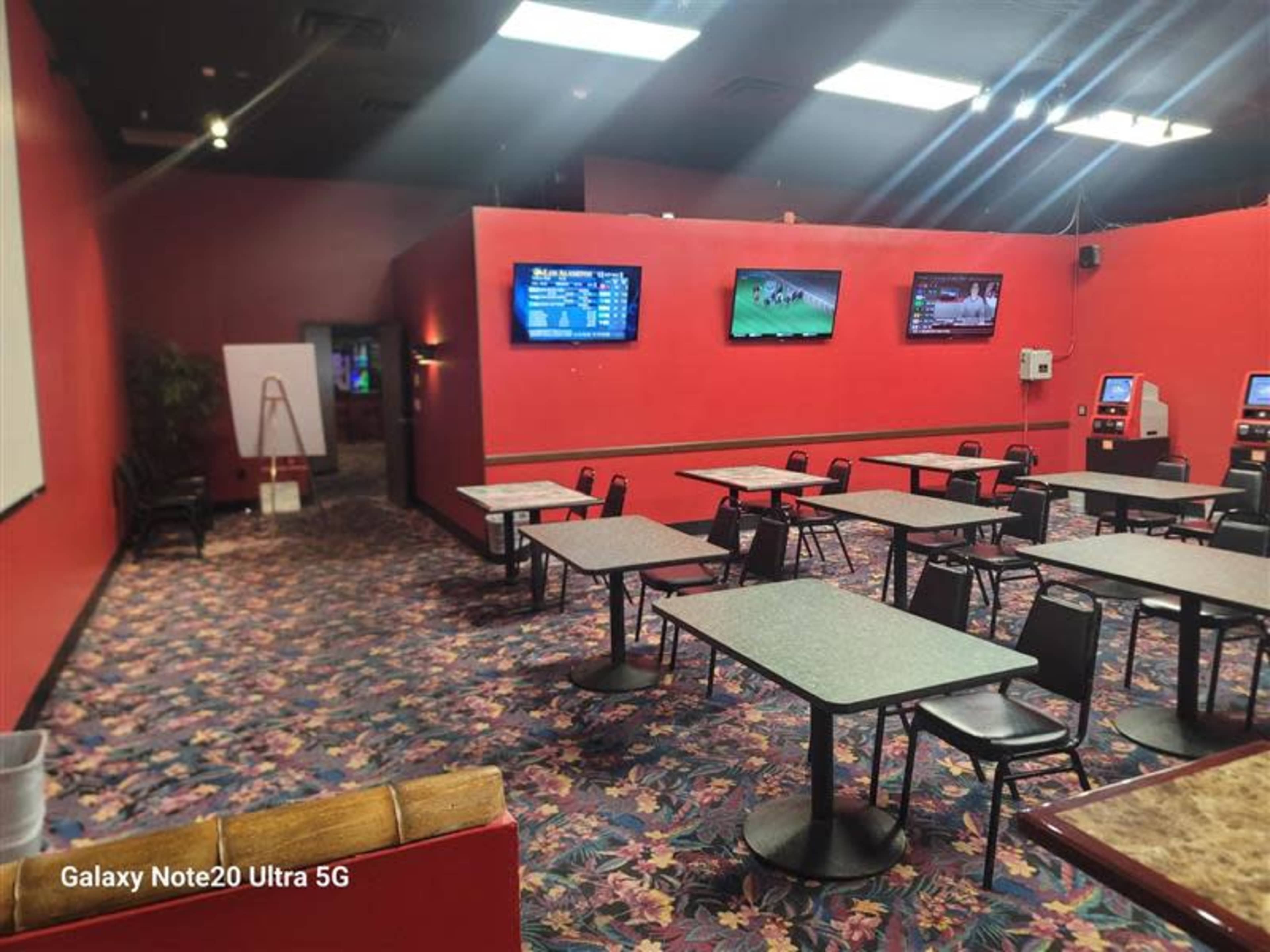 The image shows a room with red walls, several tables and chairs, and multiple screens mounted on the wall displaying various sports events.