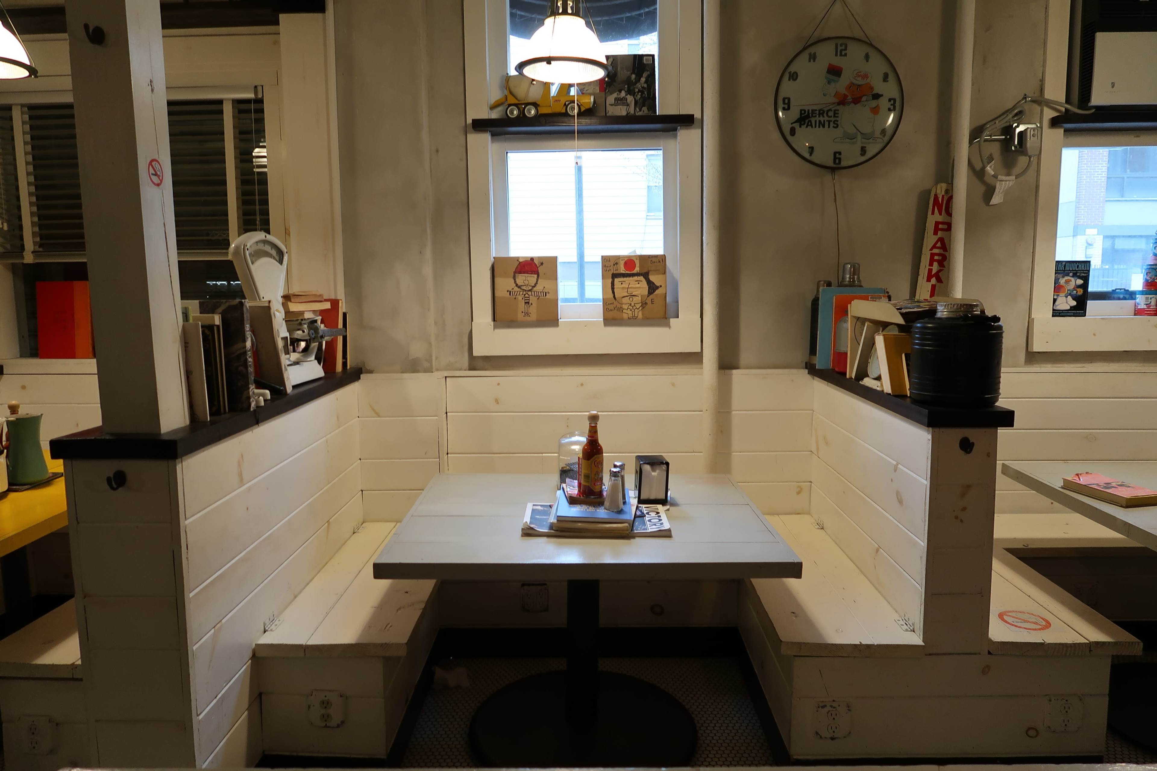 A cozy restaurant booth with a circular table surrounded by white paneling and shelves displaying various items.